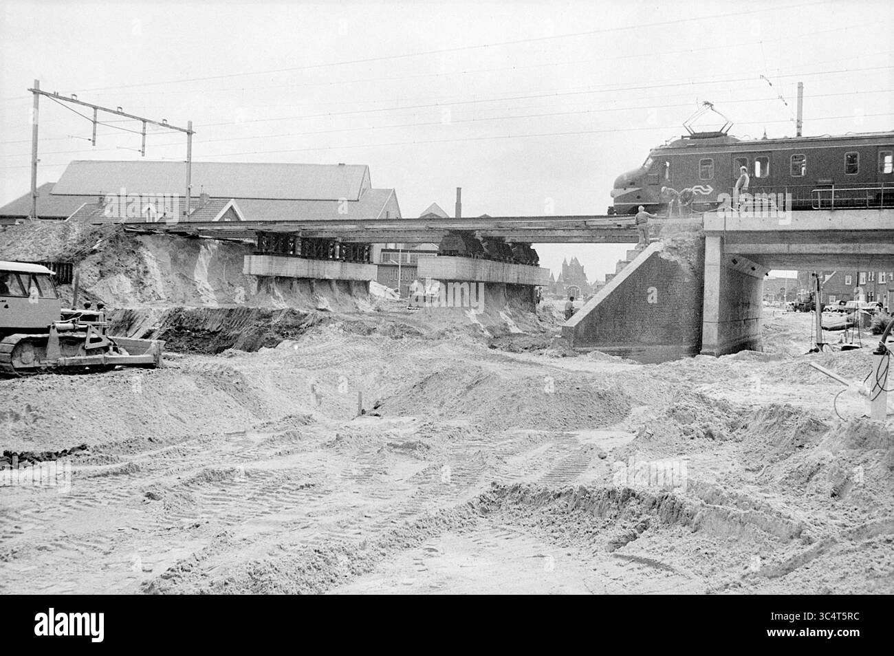 Aktivitäten Oostersingelgracht, Aktivitäten, Haarlem, Gedempte Oostersingelgracht, Niederlande, 18-06-1971 Whizgle News, Dutch Desk, Niederlande, 1950-2000 Ein Zug überquert eine teilweise erdbewegliche Brücke, die von Erdbewegungsgeräten und Bodenhaufen umgeben ist, was auf die laufende Bau- und Infrastrukturentwicklung in der Gegend hinweist. Stockfoto