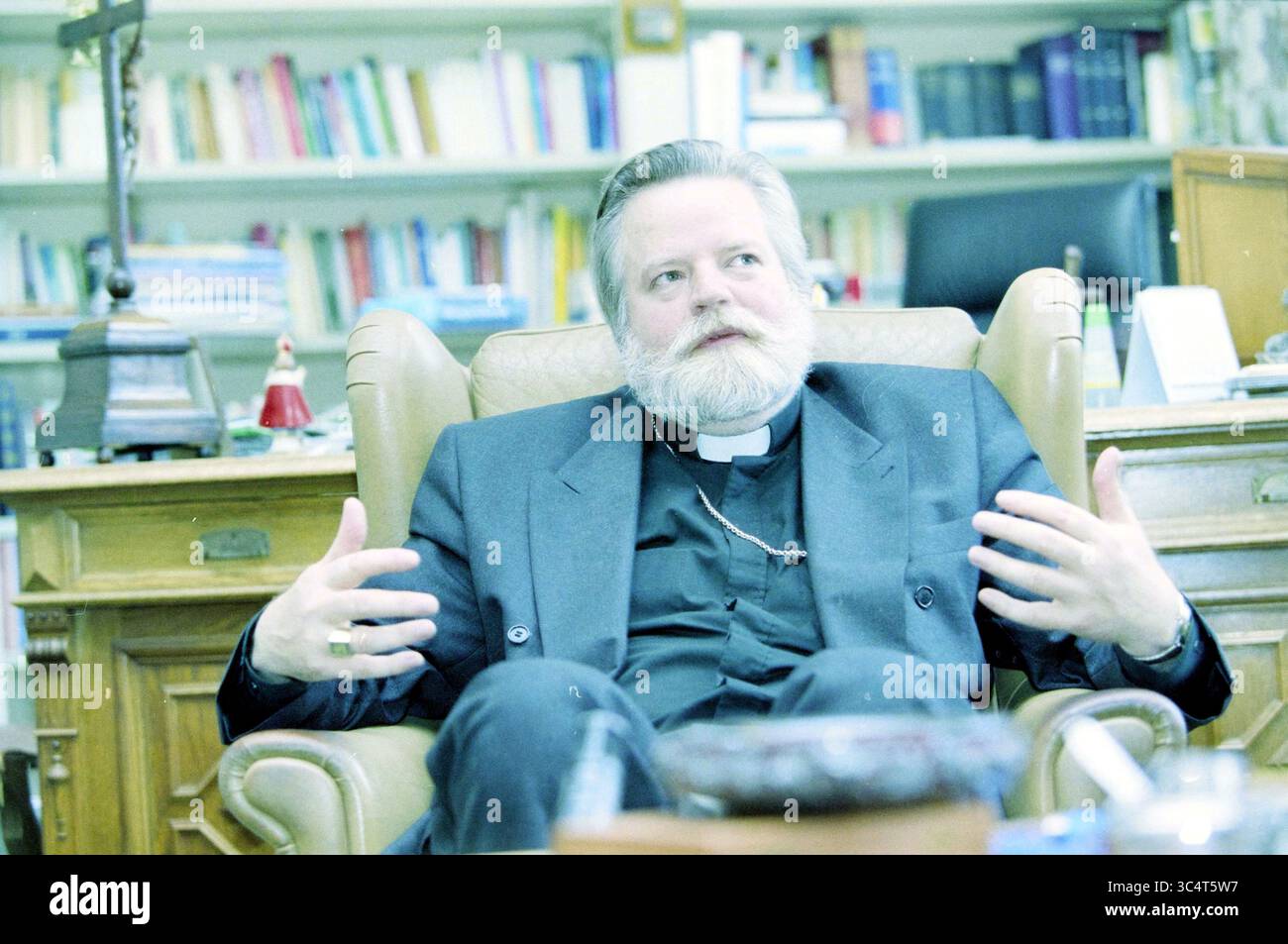 Bischof Haarlem, Mgr. Point, 01-10-2001 Whizgle News, Dutch Desk, Niederlande, 1950-2000 Ein bärtiges Geistliches sitzt nachdenklich in einem Sessel und gibt Gesten, während er ein Gespräch führt. Hinter ihm schaffen Regale, die mit Büchern und Gegenständen gesäumt sind, eine akademische Atmosphäre. Stockfoto