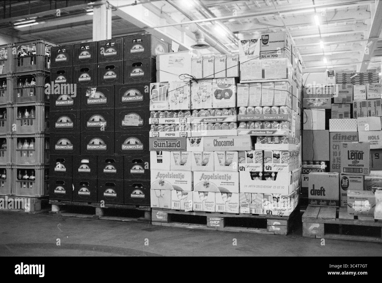 Vertriebslinien, Albert Heijn, 09-04-1991 Whizgle News, Dutch Desk, Niederlande, 1950-2000 Stapeln von übersichtlich angeordneten Kisten und Kisten säumen einen Lagerraum mit einer Vielzahl von Produkten, darunter Getränke und verpackte Waren. Die organisierten Displays legen nahe, dass der Schwerpunkt auf Bestands- und Speichereffizienz liegt. Stockfoto
