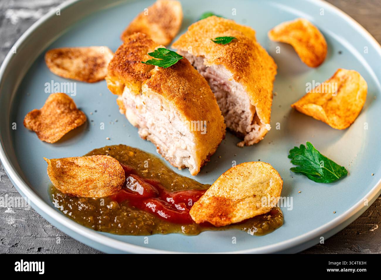 Hühnchen gefüllt mit Speck und Käse, gebraten in Lision. Ein traditionelles französisches Gericht Cordon bleu auf einem blauen Teller. Nahaufnahme. Hochwertige Fotos Stockfoto