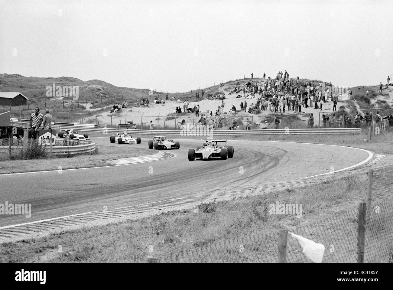 Rennstrecke Zandvoort, Zandvoort Whizgle News, Dutch Desk, Niederlande, 1950-2000 Eine Gruppe klassischer Rennwagen fährt über eine kurvenreiche Strecke, während die Zuschauer von einem Hügel im Hintergrund aus zusehen. Die Szene fängt die Spannung und Geschwindigkeit eines klassischen Motorsport-Events ein. Stockfoto