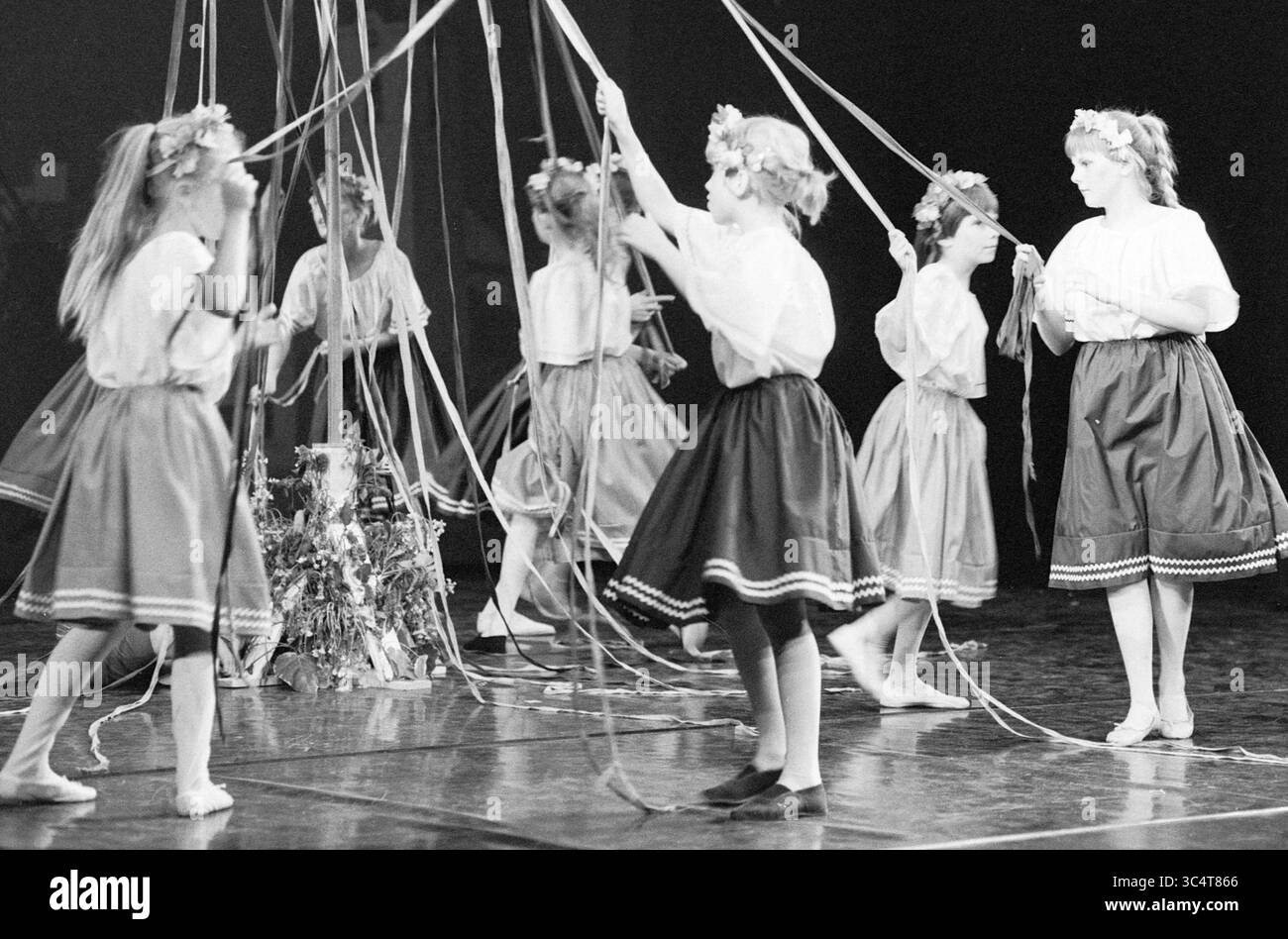 Maypole Dance Performance, 00-00-1984 Whizgle News, Dutch Desk, Niederlande, 1950-2000 Eine Gruppe junger Tänzer in traditioneller Kleidung hält anmutig bunte Bänder, die in einer synchronisierten Performance mitwirken. Ihre floralen Kopfschmuck sorgen für die festliche Atmosphäre, da sie mit den Bändern komplizierte Muster kreieren. Stockfoto