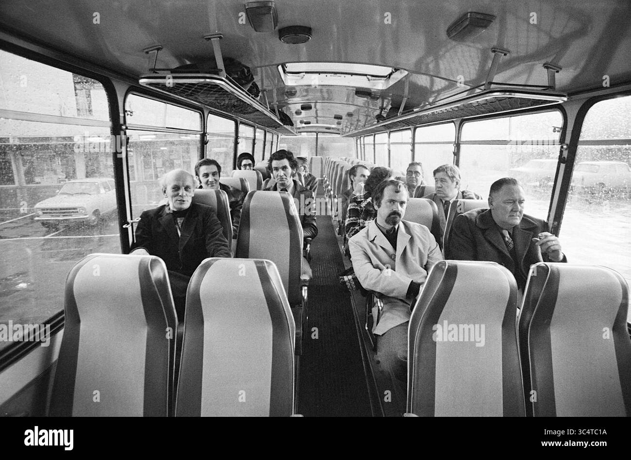 Ladenbesitzer in Heemskerk in den Haag, Leute, Geschäfte und Kioske, 28-10-1974 Whizgle News, Dutch Desk, Niederlande, 1950-2000 Eine Gruppe von Einzelpersonen sitzt in einem fast leeren Bus und zeigt eine Mischung von Ausdrücken, während sie nach vorne schauen. Die Atmosphäre lässt einen Moment der Besinnung oder der Introspektion vermuten, wobei Regen auf den Fenstern die Stimmung der Szene verstärkt. Stockfoto