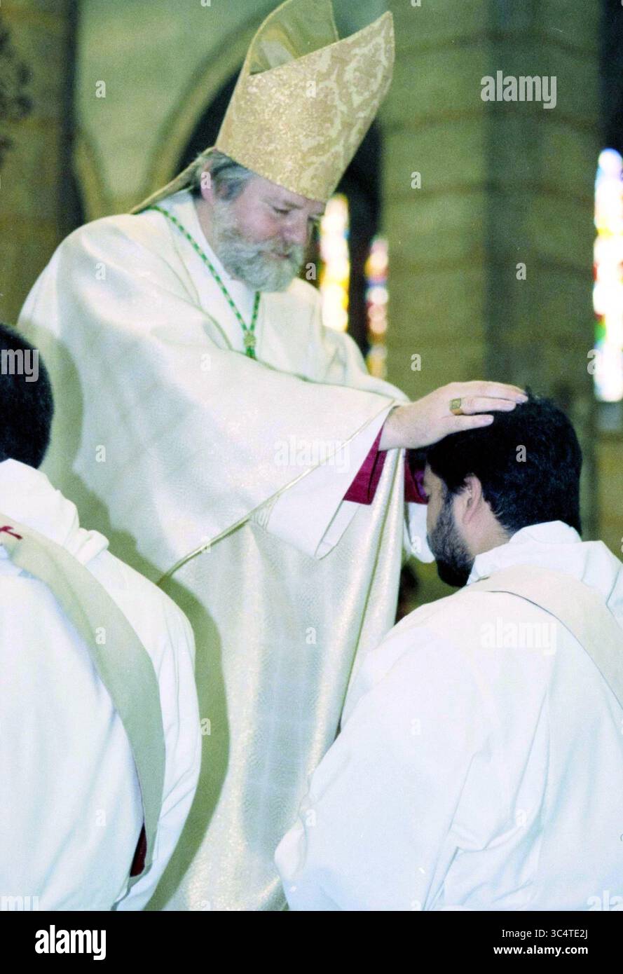 Initiation of Five Priests, 28-05-1999 Whizgle News, Dutch Desk, Niederlande, 1950-2000 Ein Geistlicher in aufwendigen Gewändern gibt einen Segen, indem er eine Hand auf den Kopf eines vor ihm knienden Individuums legt, was einen wichtigen zeremoniellen Moment anzeigt, möglicherweise die Weihe oder Bestätigung des Empfängers. Buntglasfenster sind im Hintergrund sichtbar und verleihen der Szene eine spirituelle Atmosphäre. Stockfoto