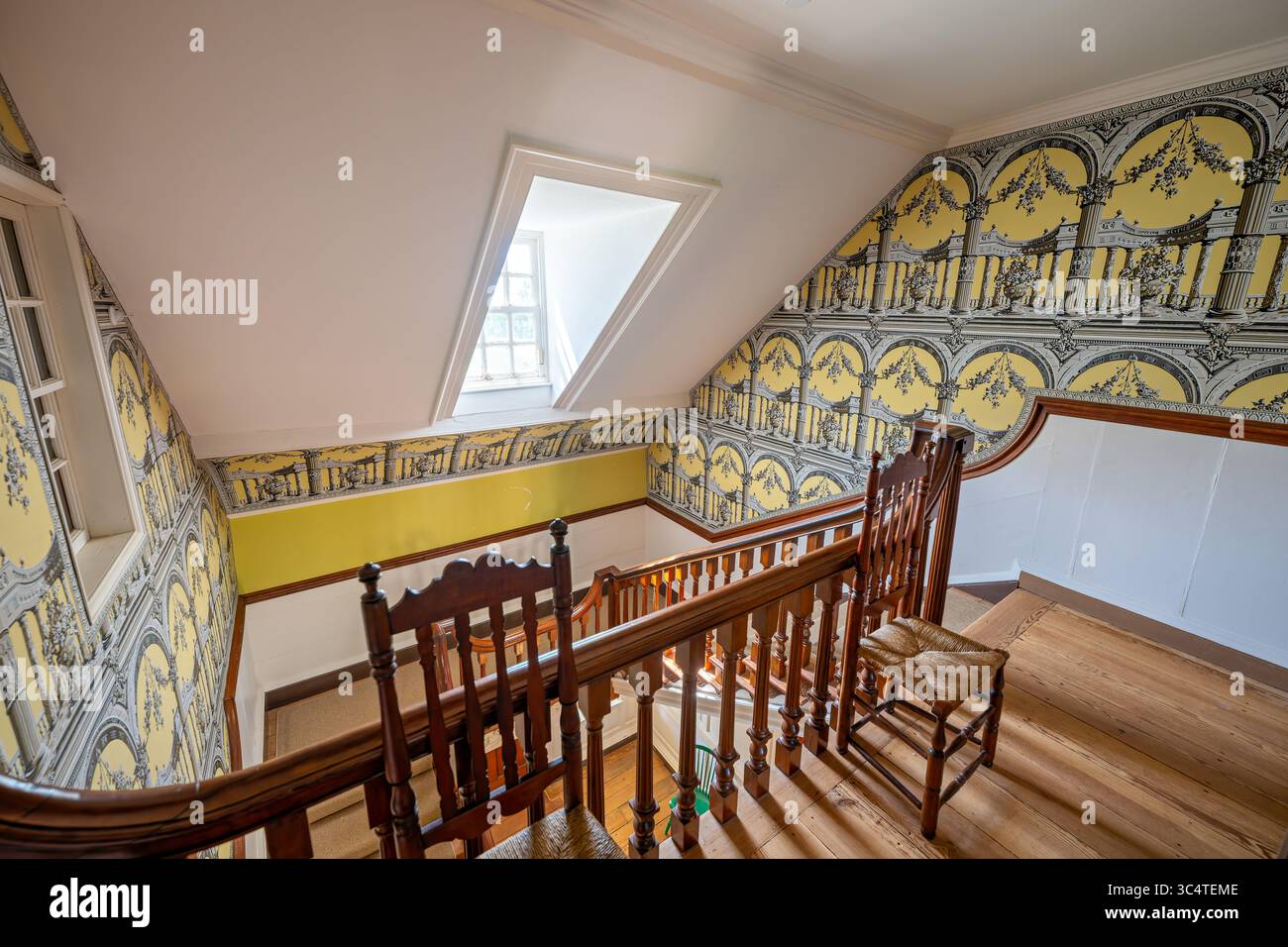 LORTON, Virginia – auf der Oberseite der Treppe in der Gunston Hall sind sorgfältig reproduzierte Säulen- und Archtapeten zu sehen, ein zeitgemäßes Muster, das auf einem englischen Design aus der Sammlung des Victoria & Albert Museums um 1769 basiert. Die Tapete mit gelbem Grund, die von Waterhouse Wallhangings mit traditionellen Holzblockdruckverfahren installiert wurde, zeigt Bogengänge mit Blumengirlanden über halbrunden Kolonnaden griechischer Säulen. Diese architektonische Tapete veranschaulicht die Trompe-l'oeil-Designs, die im England des späten 18. Jahrhunderts beliebt waren und Wohnräume in große Kolonnaden verwandelten. Gunston Ha Stockfoto
