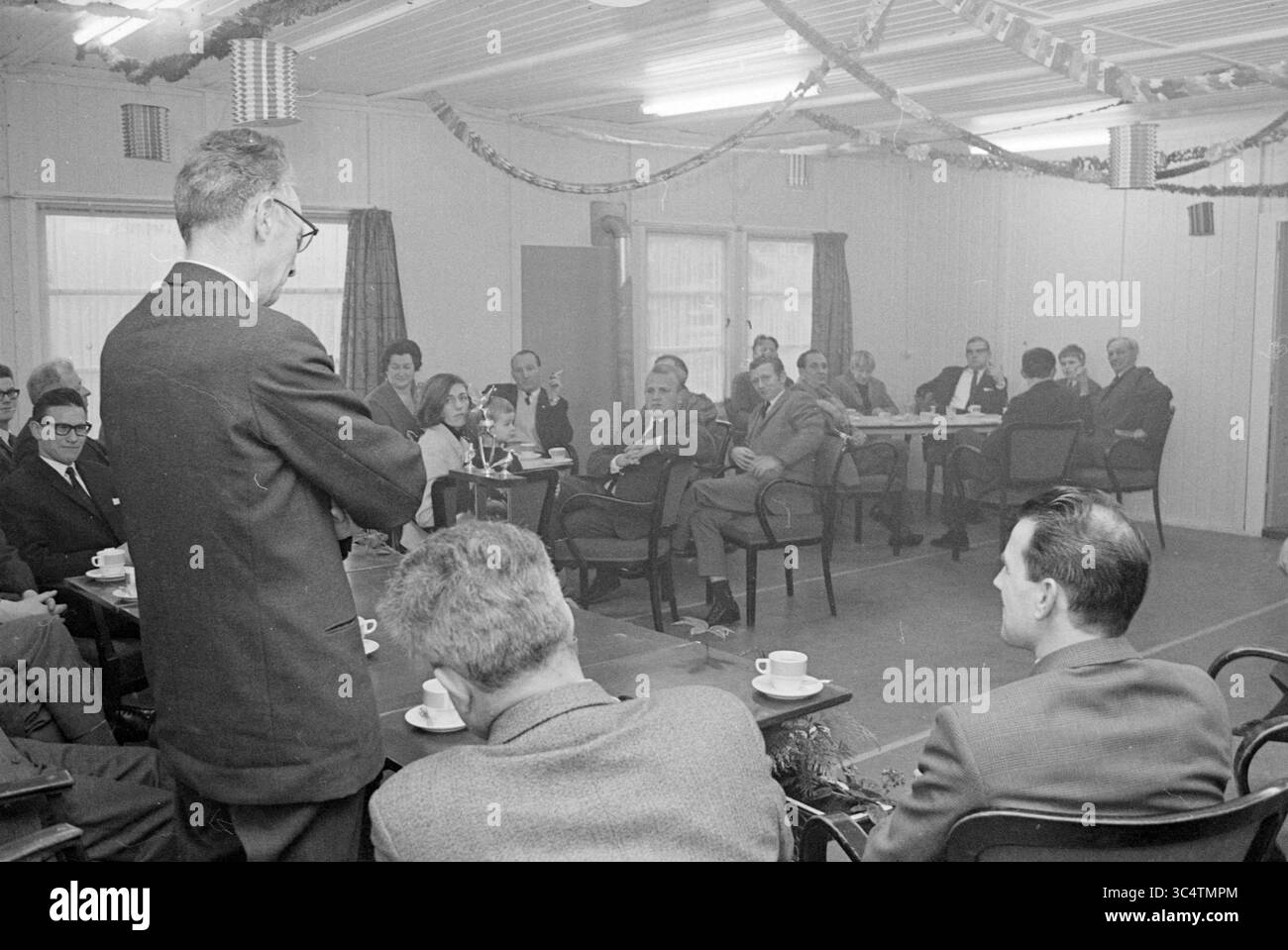 Öffnen von Luftspaltern, Öffnung, Öffnung, Inbetriebnahme, 27-01-1968 Whizgle News, Dutch Desk, Niederlande, 1950-2000 Eine Gruppe von Männern und Frauen sitzt in einem Besprechungsraum und hört aufmerksam einem Sprecher an der Vorderseite zu. Die Atmosphäre ist formell, mit Stühlen, die um kleine Tische angeordnet sind und die Teilnehmer diskutieren. Dekorationen schmücken den Raum und deuten auf einen besonderen Anlass oder eine Feier hin. Stockfoto