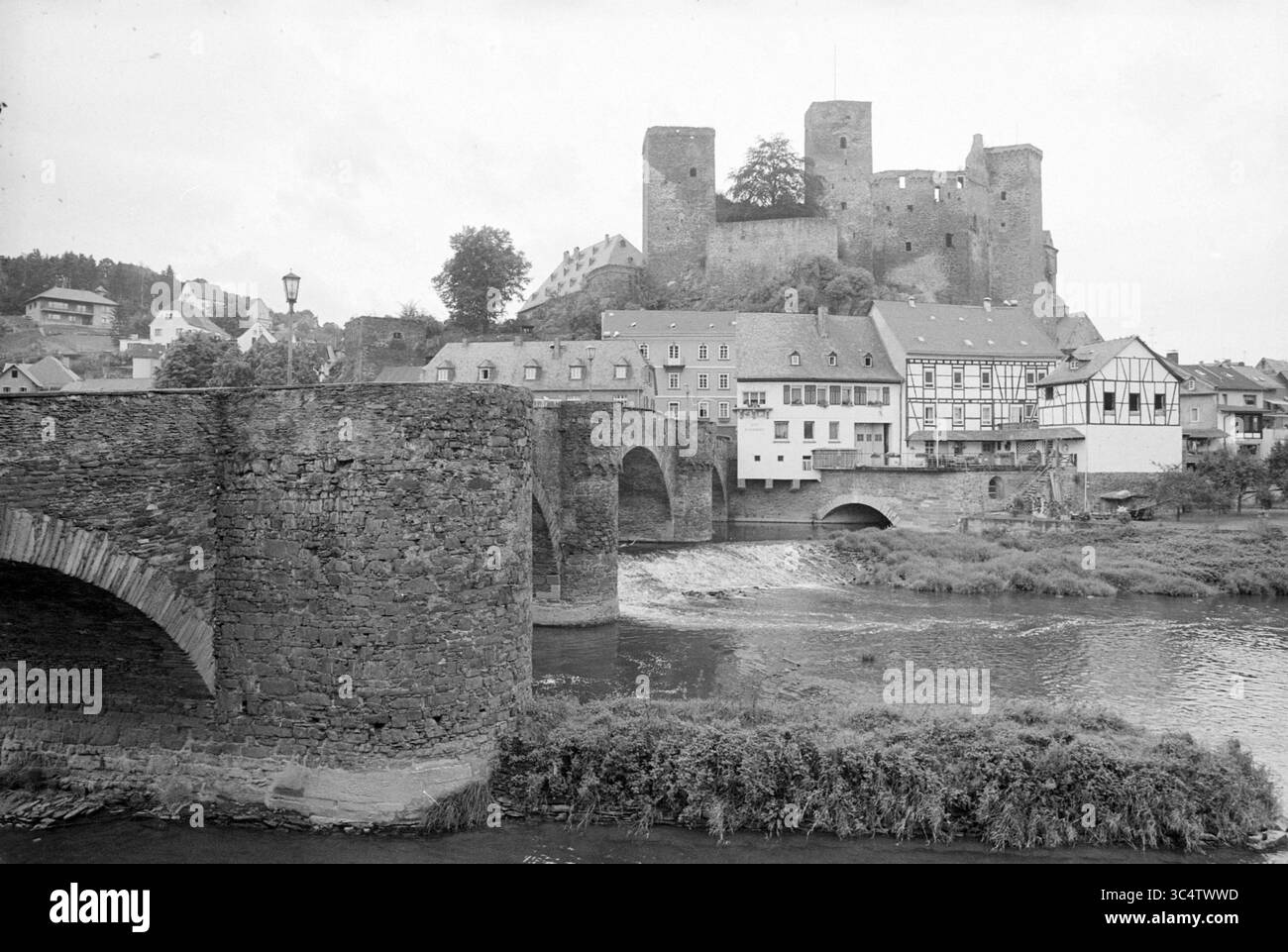 Bericht über Touristenattraktionen in Deutschland (Region Lahn), 09-09-1980 Whizgle News, Dutch Desk, Niederlande, 1950-2000 majestätisch auf einem Hügel erhebt sich Ein mittelalterliches Schloss mit Blick auf ein malerisches Dorf mit traditionellen Fachwerkhäusern. Eine stabile Steinbrücke führt über einen friedlichen Fluss und schafft eine malerische Szene, die die Harmonie zwischen Natur und Architektur unterstreicht. Stockfoto