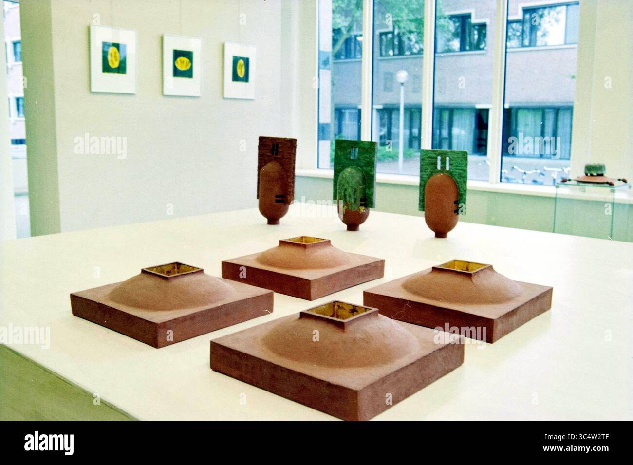 Art in de Meerse Galerie, Hoofddorp, Niederlande, 11-06-1999 Whizgle News, Dutch Desk, Niederlande, 1950-2000 eine Kunstinstallation zeigt mehrere texturierte Tonskulpturen, die auf einem Tisch angeordnet sind, ergänzt durch gerahmte Kunstwerke, die an der Wand dahinter hängen. Die Skulpturen mit verschiedenen geometrischen Formen und Öffnungen bilden einen optisch eindrucksvollen Kontrast zur Umgebung. Stockfoto