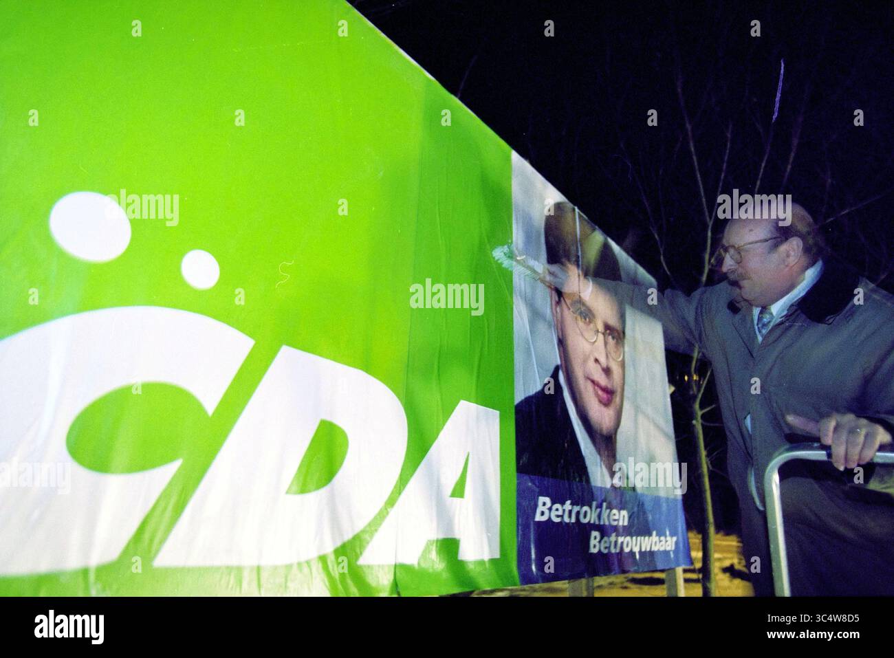 Poster CDA, Zijlweg, Overveen, Overveen, Zijlweg, 10-01-2003 Whizgle News, Dutch Desk, Niederlande, 1950-2000 Ein Mann passt ein großes Banner für eine politische Kampagne an, das das Porträt eines Kandidaten und das Logo der Partei zeigt und die Verpflichtung zu Engagement und Vertrauen unterstreicht. Stockfoto