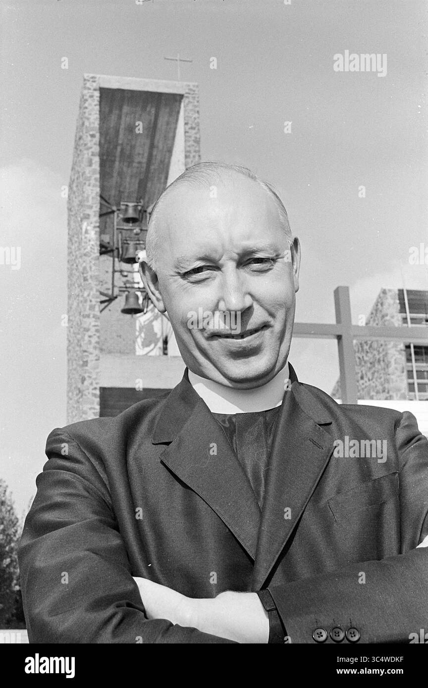Pastor Cornel, Klerus, 25-09-1969 Whizgle News, Dutch Desk, Niederlande, 1950-2000 Ein gut gekleidetes Geistliches lächelt zuversichtlich, seine Arme vor einem Kirchengebäude mit markantem Glockenturm und Kreuz im Hintergrund. Stockfoto