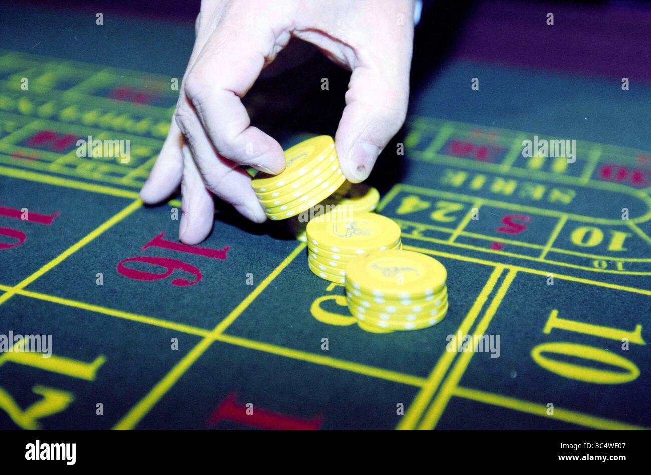 Casino Whizgle News, Dutch Desk, Niederlande, 1950-2000 Eine Hand platziert gelbe Poker-Chips auf einem Wetttisch, was den Nervenkitzel des Glücksspiels und die Erwartung eines Spiels unterstreicht. Stockfoto