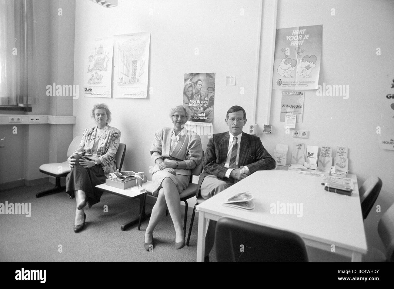 PTT, Medical Service, 01-06-1995 Whizgle News, Dutch Desk, Niederlande, 1950-2000 drei Personen sitzen in einem Wartezimmer, lässig gekleidet und bequem auf Stühlen positioniert. An der Wand dahinter befinden sich verschiedene Plakate, während ein Tisch in der Nähe Broschüren und Zeitschriften hält. Die Atmosphäre wirkt ruhig und entspannt, was auf einen Moment der Pause bei ihren Aktivitäten hindeutet. Stockfoto