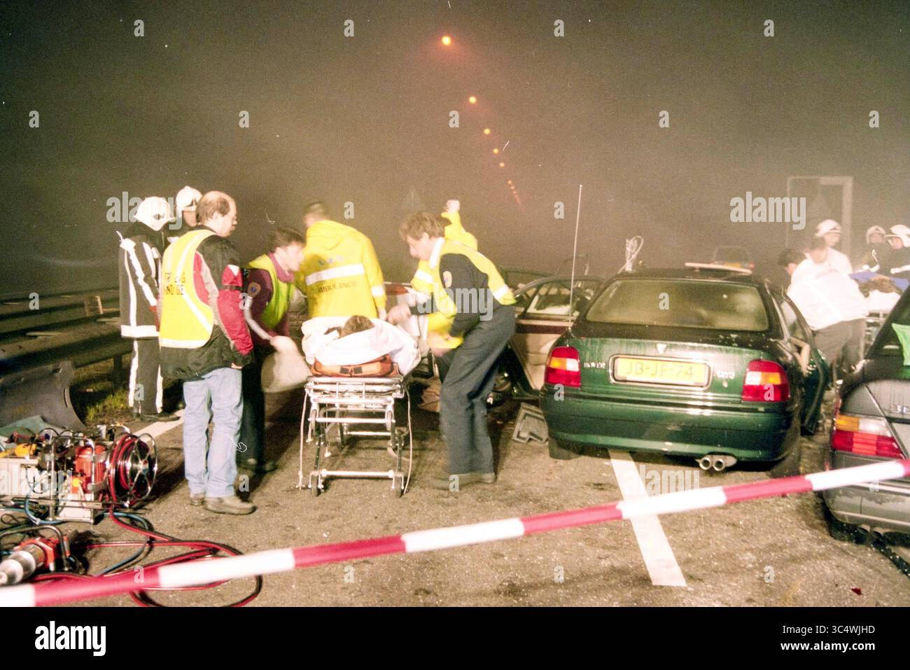 Unfall durch Nebel auf der A4, Rijksweg A4, 31-12-1997, Whizgle News, Dutch Desk, Niederlande, 1950-2000 Notfallhelfer kümmern sich um einen schweren Unfall mit mehreren Fahrzeugen auf einer Autobahn. Einige Menschen werden unterstützt, während andere auf einer Bahre transportiert werden, inmitten einer Nebelszene. Der Verkehr wird gestoppt, wenn sich die Rettungsmaßnahmen entfalten. Stockfoto