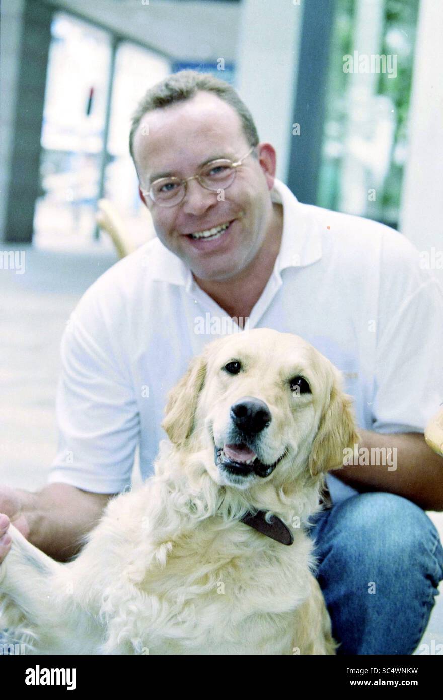 Porträt von Mann mit Hund Whizgle News, Dutch Desk, Niederlande, 1950-2000 Ein lächelnder Mann sitzt bequem und interagiert spielerisch mit einem fröhlichen Golden Retriever, beide genießen einen Moment der Gemeinschaft. Stockfoto