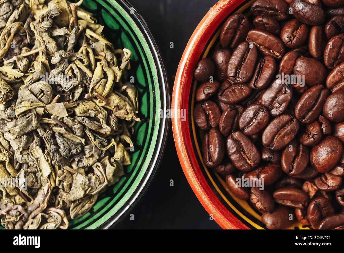 Kaffeebohnen und Teeblätter. Kontrast zwischen dunklem Braten und getrockneten Kräutern. Getränkezutaten flach aufgelegt. Natürlicher Texturhintergrund. Warme Erdfarbe Stockfoto