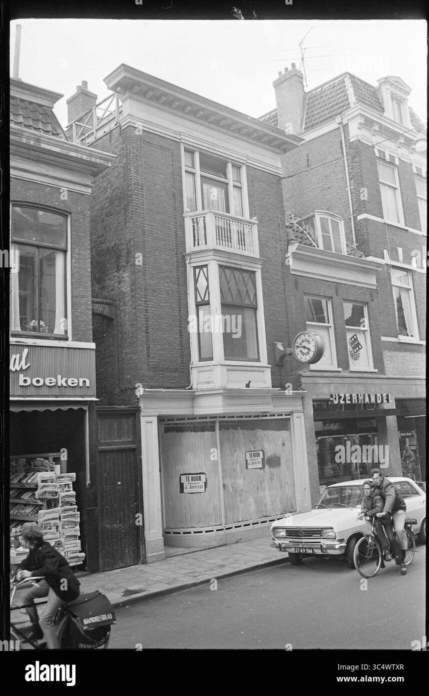 Geschäfte in der Kruisstraat in Haarlem: Unter der Nummer 40 de Boekhal für Bücher und Zeitschriften, unter der Nummer 38 ein Mietgebäude, in dem sich Moors befand (Funktechnikfirma) und unter der Nummer 34-36 IJzerhandel Schaap., Haarlem, Kruisstraat, The Netherlands Whizgle News, Dutch Desk, Niederlande, 1950-2000 Eine Straßenszene mit einem zweistöckigen Backsteingebäude mit markanten Balkon, flankiert von Schaufensterfronten mit Büchern und einem Schild für Ein Café. Ein Radfahrer fährt vorbei, während in der Nähe ein Zeitungskiosk voller Zeitungen zu sehen ist. Stockfoto