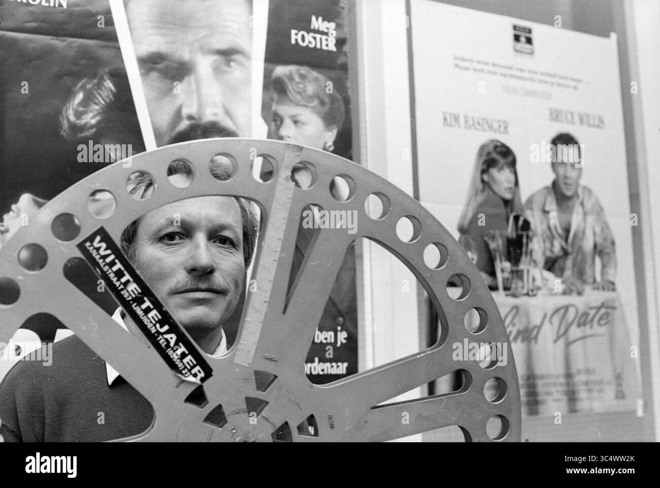 Herman de Groot, IJmuiden, IJmuiden, Niederlande, 17-04-1991 Whizgle News, Dutch Desk, Niederlande, 1950-2000 Ein Mann hält eine große Filmrolle vor sich, eingerahmt von Vintage-Filmplakaten mit bekannten Stars. Die Szene weckt ein Gefühl von Nostalgie für das klassische Kino. Stockfoto