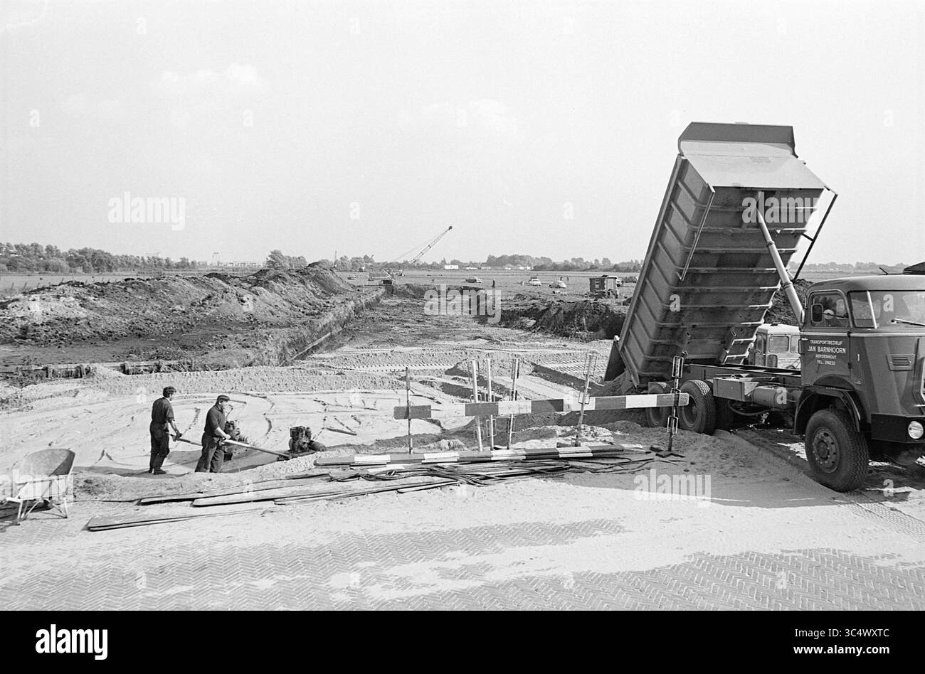 Chimney Broekerpolder, Works, 23-09-1969 Whizgle News, Dutch Desk, Niederlande, 1950-2000 Bauarbeiter beaufsichtigen das Entladen von Materialien aus einem Müllwagen an einem Standort mit Erdbewegungsmaschinen und laufenden Aushubarbeiten vor dem Hintergrund weit entfernter Maschinen und eines klaren Himmels. Stockfoto