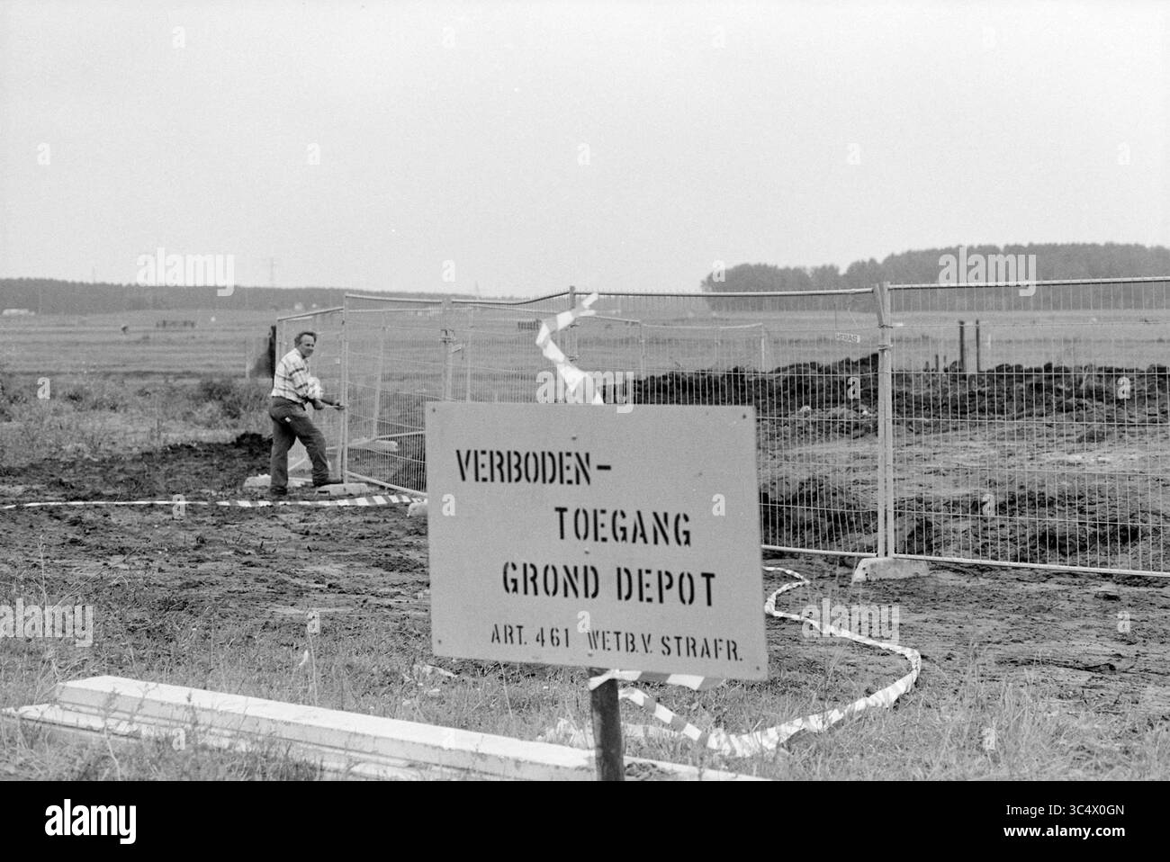 Treibsand Terrain, Velserbroek, 01-09-1993 Whizgle News, Dutch Desk, Niederlande, 1950-2000 Eine Baustelle mit einem auffälligen Schild, das auf eingeschränkten Zugang hinweist, während ein Arbeiter im Hintergrund die Umzäunung anpasst. Der Ort scheint in einem ländlichen Gebiet zu liegen, mit weit entfernten Bäumen am Horizont. Stockfoto