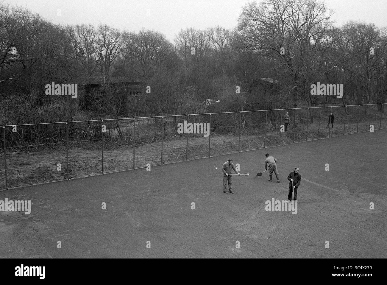 Whizgle News, Dutch Desk, Niederlande, 1950-2000 Eine Gruppe von Einzelpersonen beschäftigt sich mit Gartenarbeiten und räumt einen umzäunten Bereich ein, der von kargen Bäumen und bewachsenen Büschen umgeben ist, was auf den Beginn des Frühlings und die Restaurierung eines Erholungsraums hindeutet. Stockfoto