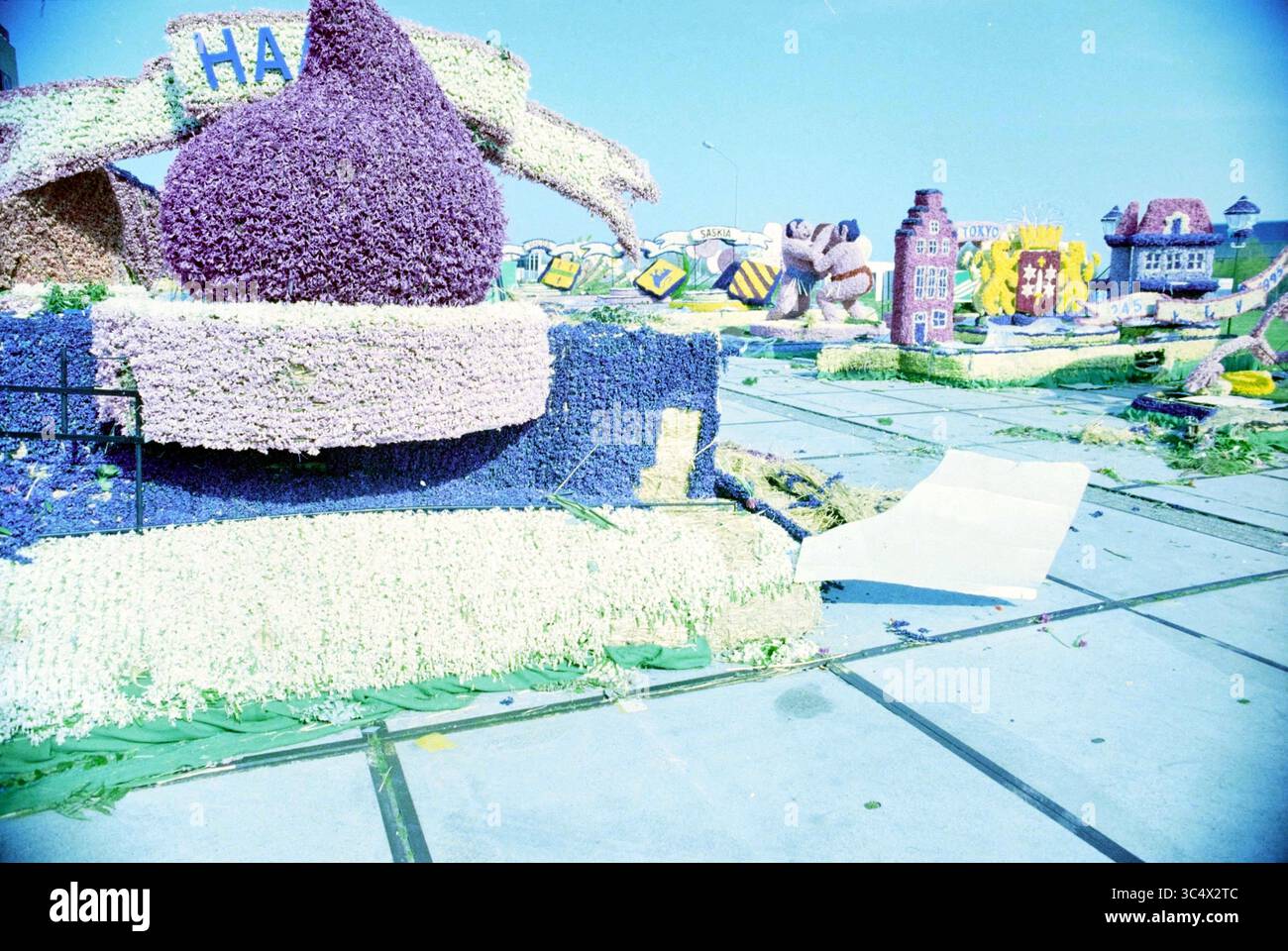 Waggons parkten auf einem Industriegebiet nach der Blumenparade, Haarlem, Niederlande, 23-04-1995 Whizgle News, Dutch Desk, Niederlande, 1950-2000 Ein lebendiges Schauspiel von aufwendig gestalteten Blumenmotiven und Dekorationen mit verschiedenen skurrilen Formen und Farben vor einem hellen Himmel. Die Szene ist voller kreativer Elemente, einschließlich überdimensionaler Darstellungen von Tieren und Gebäuden, die zu einer festlichen Atmosphäre beitragen. Stockfoto