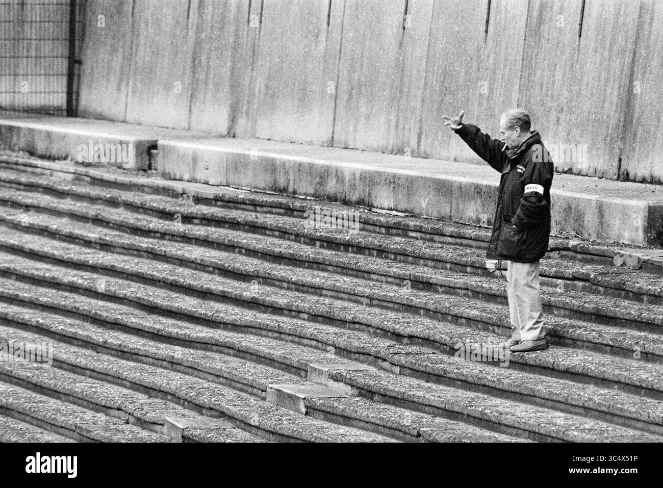 Leere Stadium, Haarlem, Niederlande, 03-09-1993 Whizgle News, Dutch Desk, Niederlande, 1950-2000 ein älterer Mann steht allein auf einer Reihe von gestuften Schritten, indem er Gesten macht, als ob er sich unterhalten oder einen Gedanken ausdrückt. Die Strenge der Inszenierung betont seine einsame Figur gegen die sich wiederholenden Linien der Stufen um ihn herum. Stockfoto Leere Stadium, Haarlem, Niederlande, 03-09-1993 Whizgle News, Dutch Desk, Niederlande, 1950-2000 ein älterer Mann steht allein auf einer Reihe von gestuften Schritten, indem er Gesten macht, als ob er sich unterhalten oder einen Gedanken ausdrückt. Die Strenge der Inszenierung betont seine einsame Figur gegen die sich wiederholenden Linien der Stufen um ihn herum. Stockfoto
