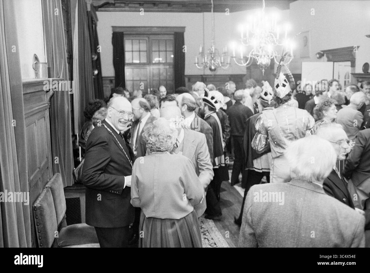 Neujahrsempfang Zandvoort, Neujahrsempfänge, Zandvoort, 04-01-1988 Whizgle News, Dutch Desk, Niederlande, 1950-2000 Ein lebhaftes Treffen von Gesprächspartnern, in formeller Kleidung, mit einigen Gästen, die bunte Kostüme und Kronen tragen. Das Ambiente ist warm, mit eleganten Kronleuchtern und Holzmöbeln. Stockfoto