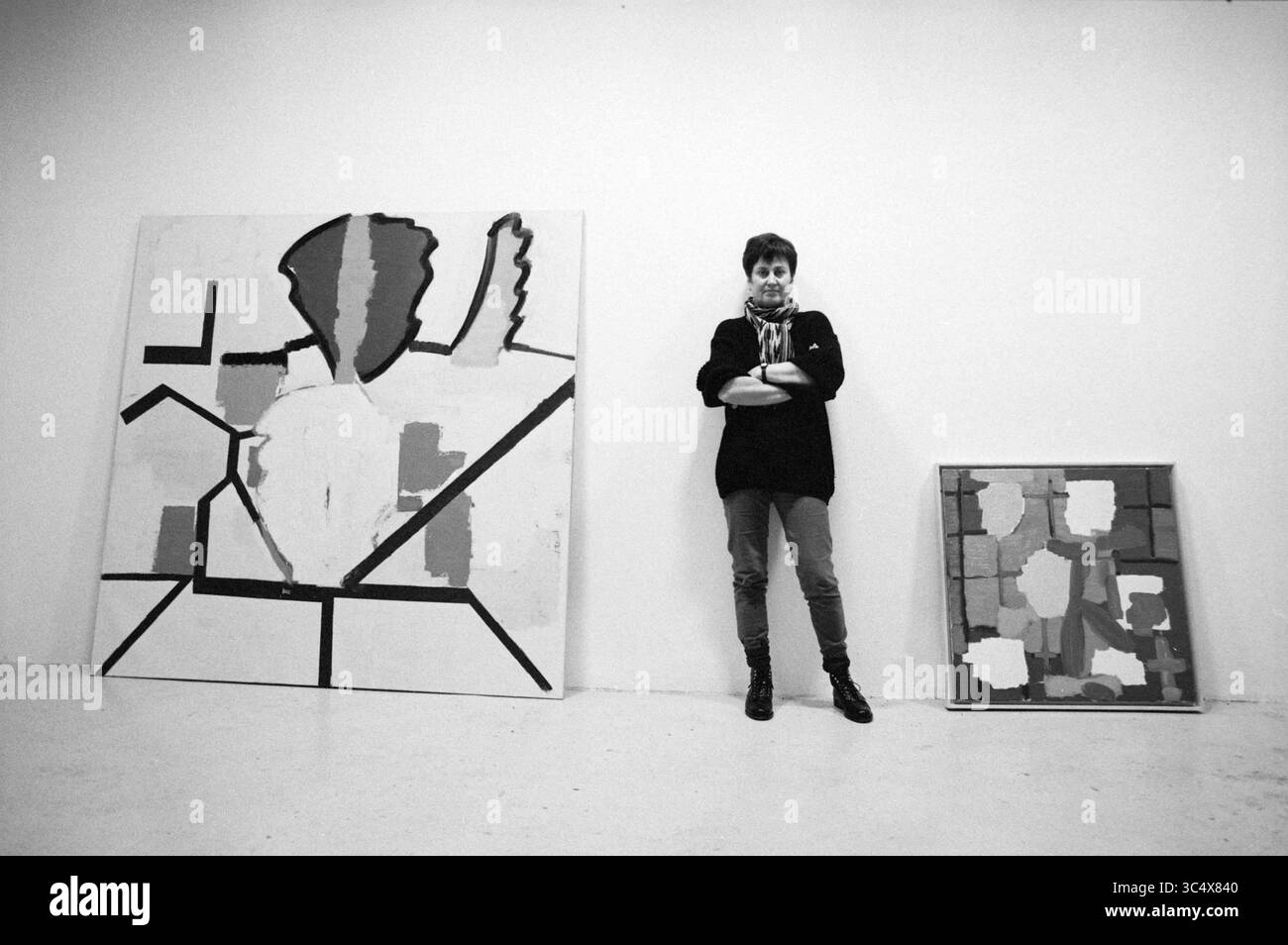 Hanny Bannink, Kaaij Gallery, 07-12-1993 Whizgle News, Dutch Desk, Niederlande, 1950-2000 ein Künstler steht selbstbewusst neben zwei abstrakten Gemälden, die kräftige Formen und einen Farbmix zeigen. Der Künstler trägt ein stilvolles Outfit mit überkreuzten Armen, was zur kreativen Atmosphäre des Raumes beiträgt. Stockfoto