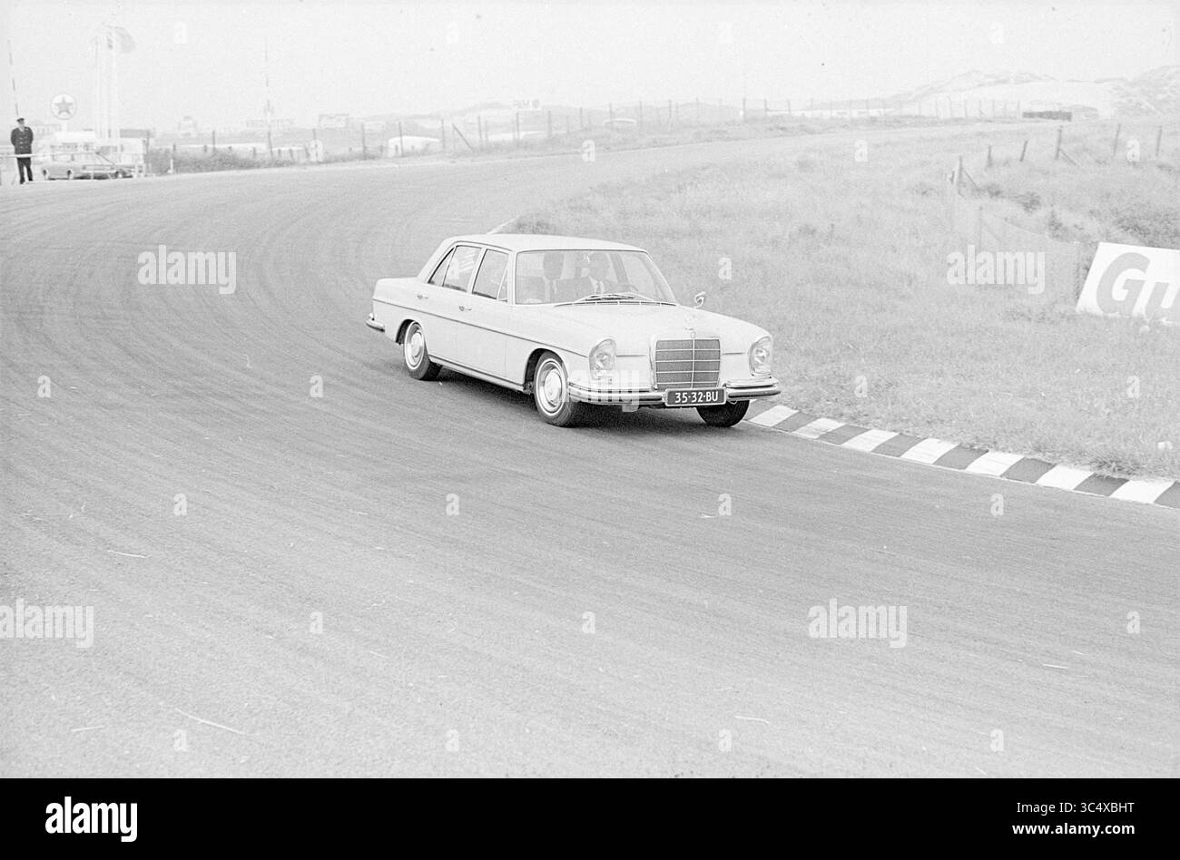 Ein Mercedes auf der Rennstrecke von Zandvoort, Zandvoort Whizgle News, Dutch Desk, Niederlande, 1950-2000 Eine klassische Limousine navigiert auf einer Rennstrecke durch die Kurve und zeigt ihr elegantes Design und ihren Vintage-Charme. Im Hintergrund deuten ferne Figuren und Fahrzeuge auf ein Ereignis hin. Stockfoto