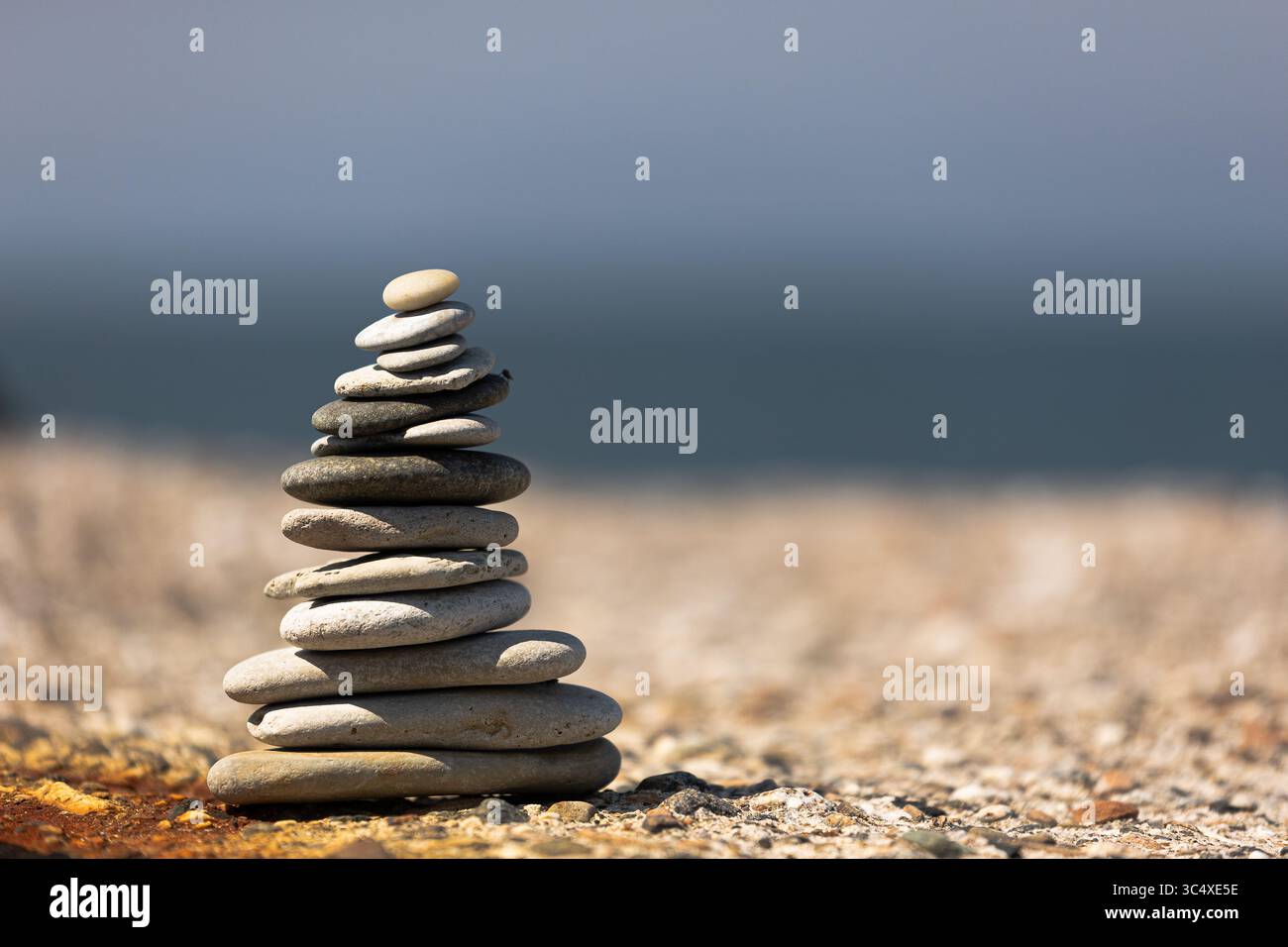 Gestapelte Kieselsteine balanciert an einem Sandstrand mit dem Meer im Hintergrund, symbolisieren Frieden, Gleichgewicht und Achtsamkeit in der Natur. Stockfoto