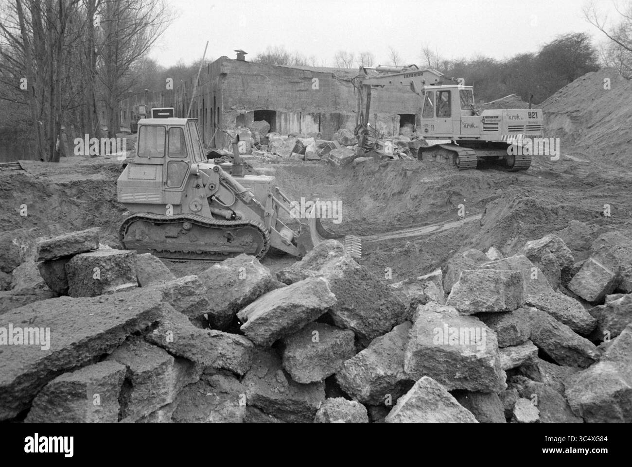 Teilweiser Abriss von Fort Velsen der Verteidigungslinie von Amsterdam, Velsen, 08-01-1981 Whizgle News, Dutch Desk, Niederlande, 1950-2000 Baumaschinen arbeiten in einer Landschaft aus zerbrochenem Beton und Schutt, während die Überreste eines Bauwerks im Hintergrund stehen. Bäume säumen den Horizont und setzen einen starken Kontrast zur Szene des Abbruchs und der Erdbewegung. Stockfoto
