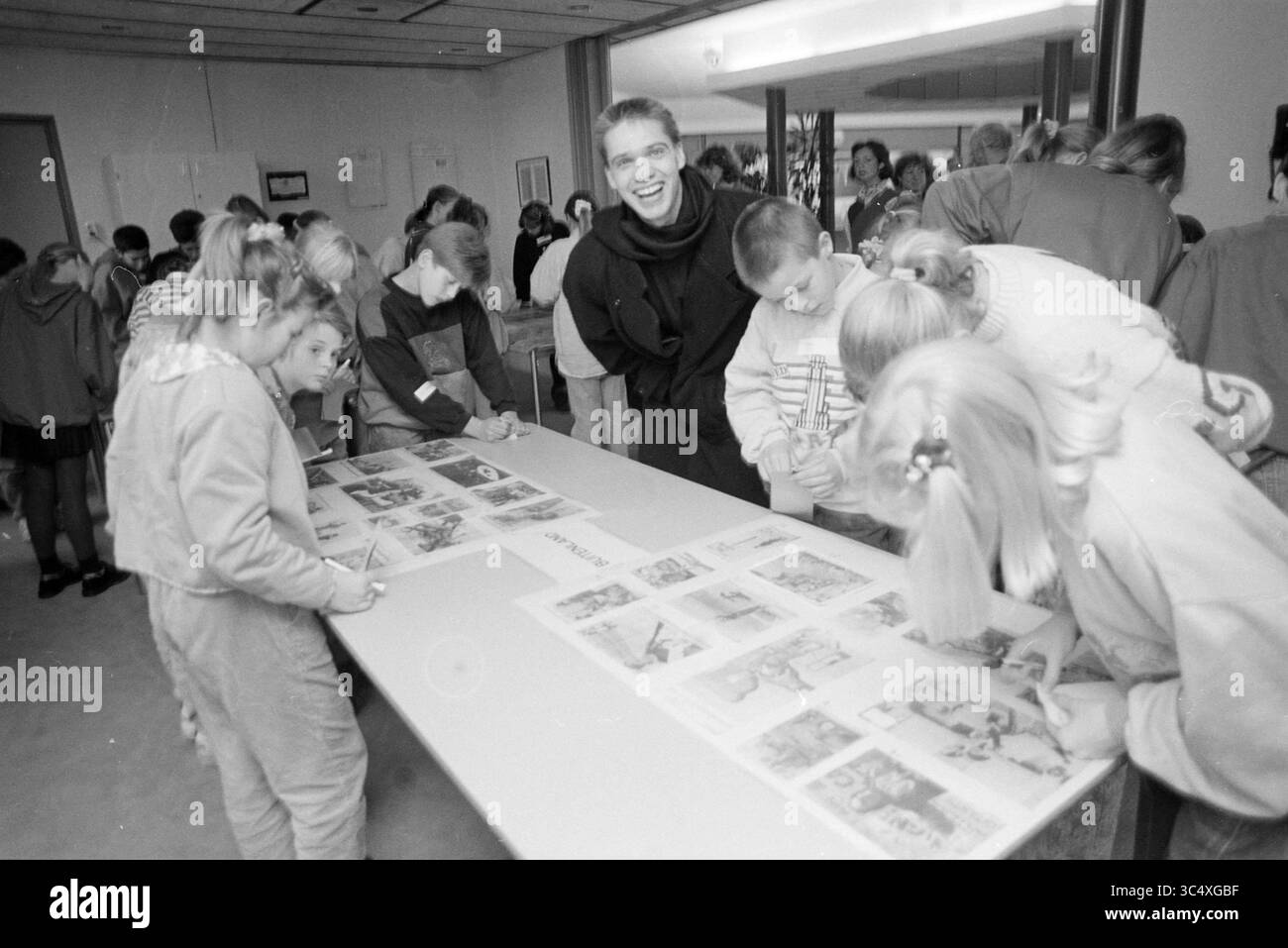 Kinder-Richter-Zeitungsfoto, 26-11-1991 Whizgle News, Dutch Desk, Niederlande, 1950-2000 Eine lebhafte Gruppe von Kindern versammelt sich an einem Tisch, um an einem Kunstprojekt teilzunehmen. Sie konzentrieren sich auf das Ausmalen und Zeichnen auf die vor ihnen liegenden Blätter, während ein Erwachsener im Hintergrund ein fröhliches Lächeln teilt, was zur lebhaften Atmosphäre der Kreativität und Freude beiträgt. Stockfoto