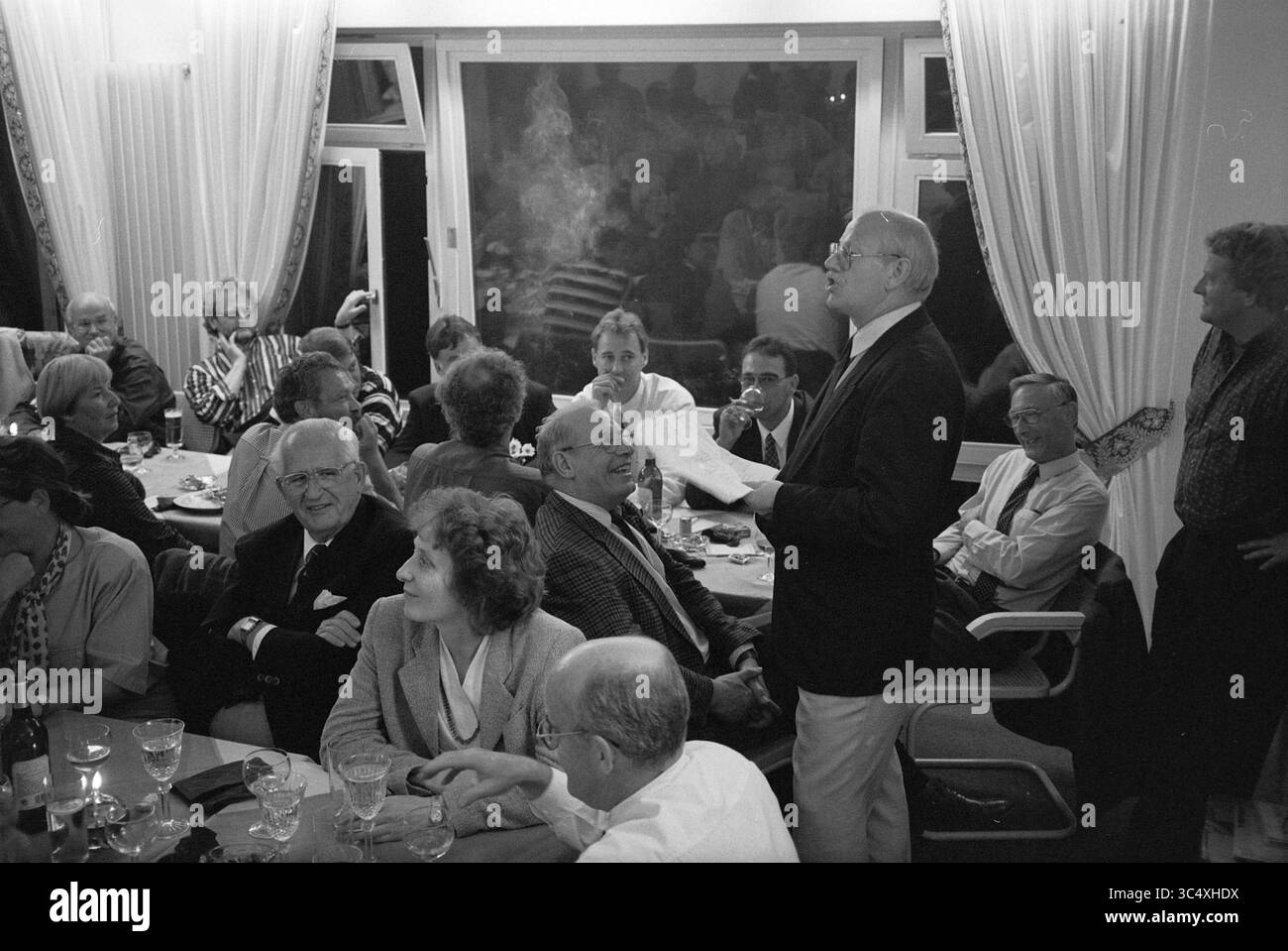 Mr. Besselink, Amateurbier, 27-09-1994 Whizgle News, Dutch Desk, Niederlande, 1950-2000 Eine Zusammenkunft von mehreren Personen, die an einem Tisch lebhafte Gespräche führen, wobei eine Person steht und mit der Gruppe spricht. Die Atmosphäre ist warm und einladend, voller Lachen und Kameradschaft, während die Teilnehmer Drinks und gemeinsame Momente genießen. Stockfoto