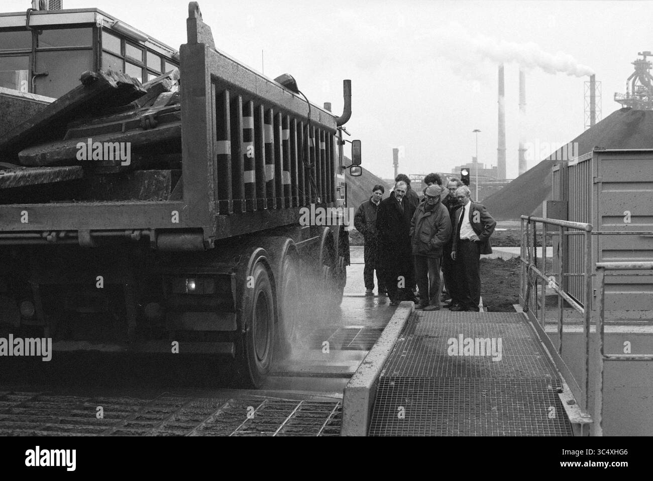 Führung @@, Hoogovens [techn.], Utrecht, 24-11-1992 Whizgle News, Dutch Desk, Niederlande, 1950-2000 Eine Gruppe von Arbeitnehmern beobachtet einen großen Lkw beim Entladen von Materialien an einem Industriegelände, wobei im Hintergrund Fabrikschornsteine und Rohstoffhaufen stehen. Stockfoto