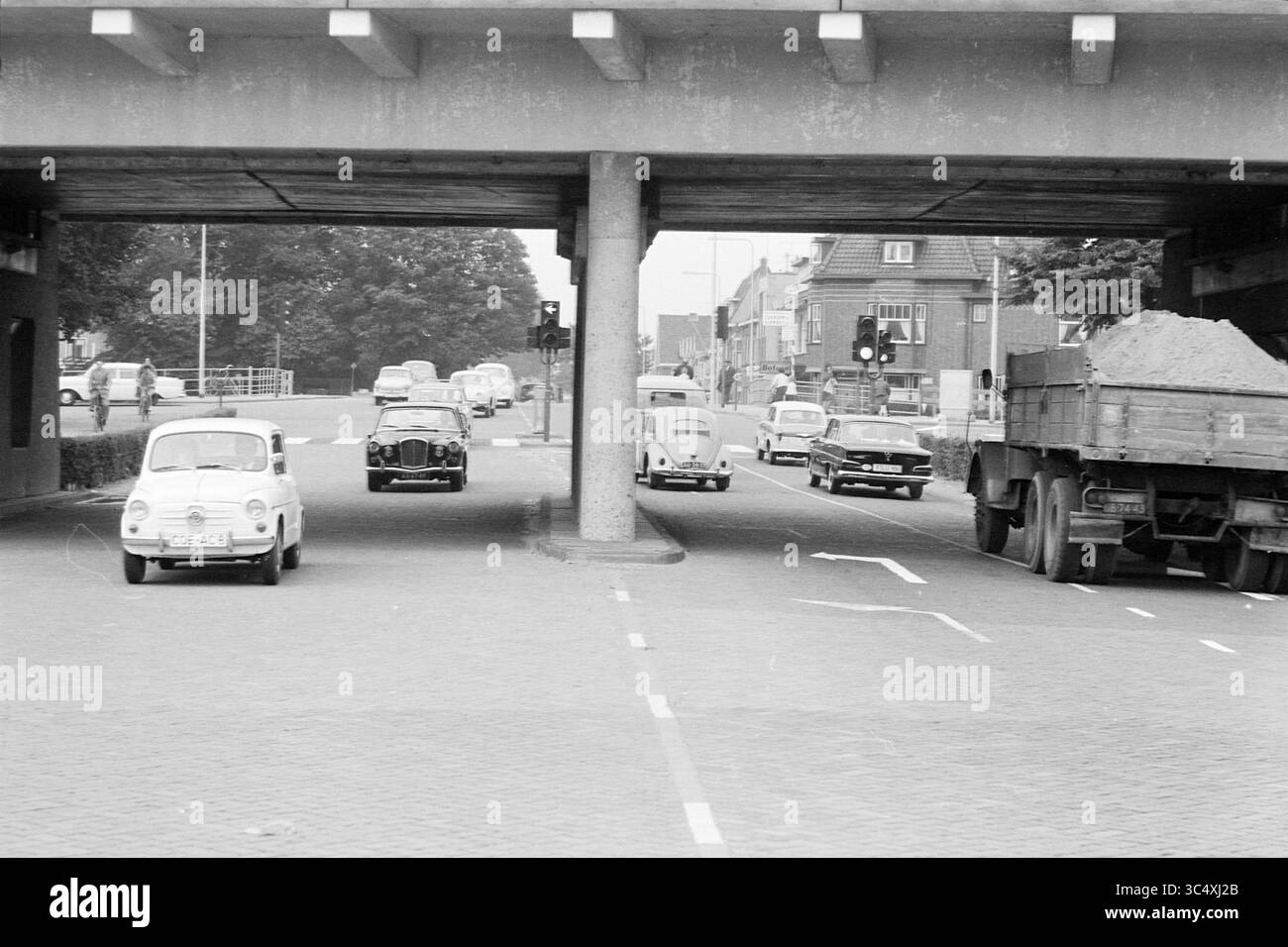 Crossroads Zandvoortselaan Leidsevaart, Traffic, sicherer Verkehr, 05-08-1963 Whizgle News, Dutch Desk, Niederlande, 1950-2000 Eine geschäftige Kreuzung mit Oldtimern und einem großen Lkw, der unter einer Betonüberführung vorbeifährt, mit sichtbaren Verkehrszeichen und Bäumen am Hintergrund. Stockfoto
