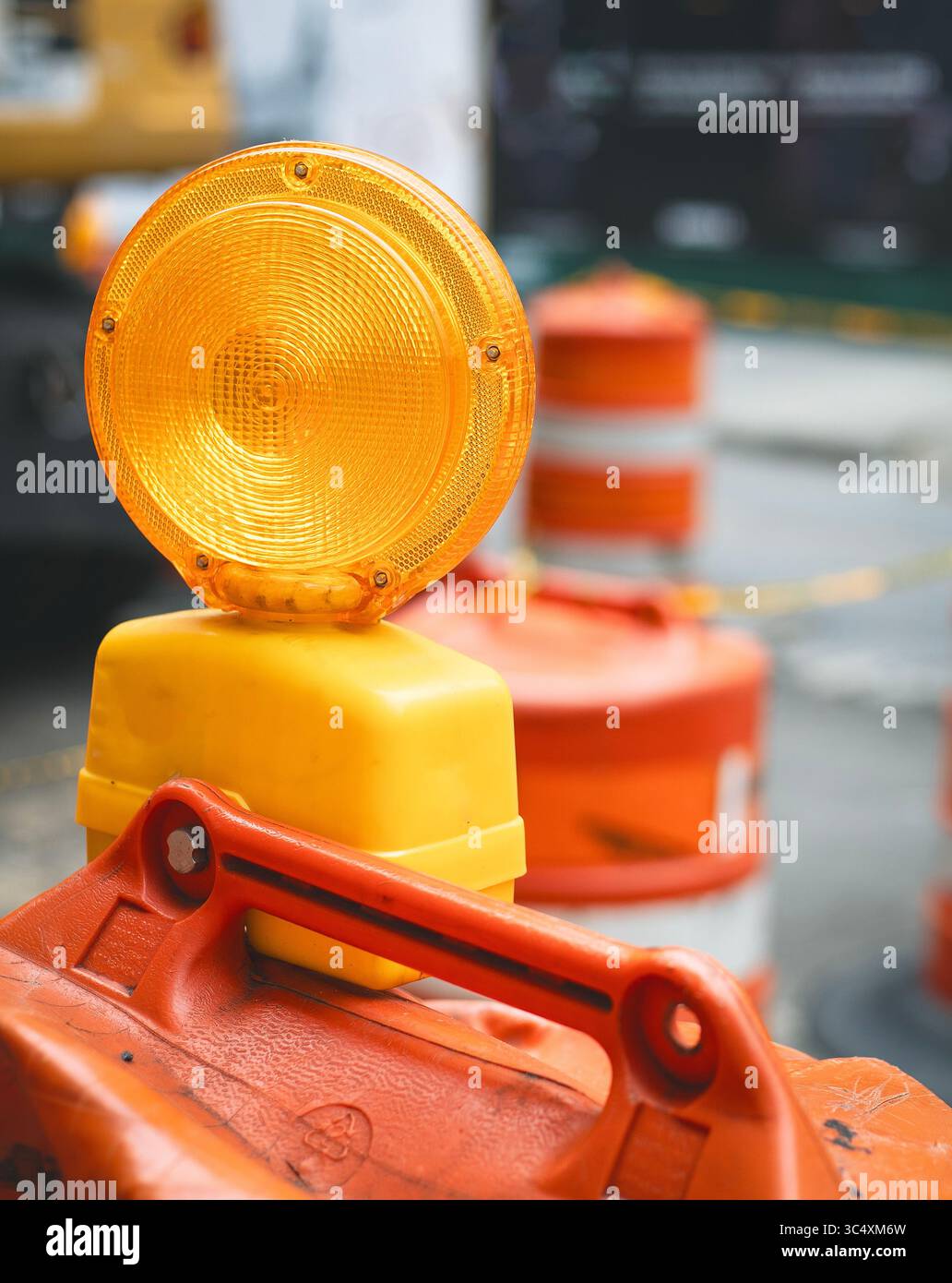 Eine hellgelbe Warnleuchte befindet sich auf einer orangefarbenen Verkehrsbarrikade, die die Präsenz in einem Baubereich unterstreicht. Stockfoto