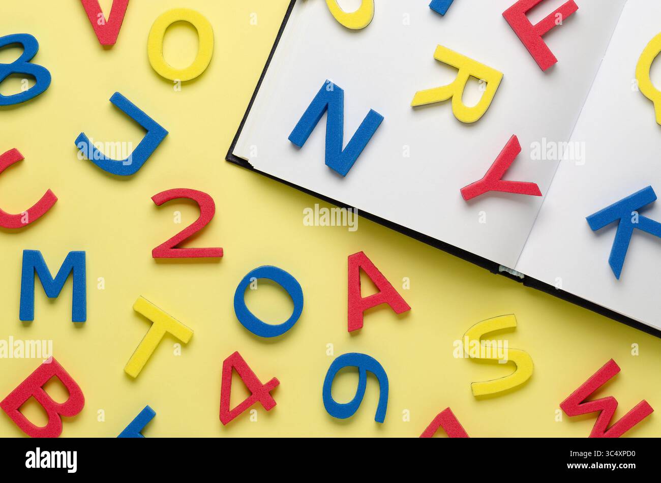 Ein Notizbuch und bunte Buchstaben und Zahlen auf hellgelbem Hintergrund. Back-to-School-Konzept. Stockfoto