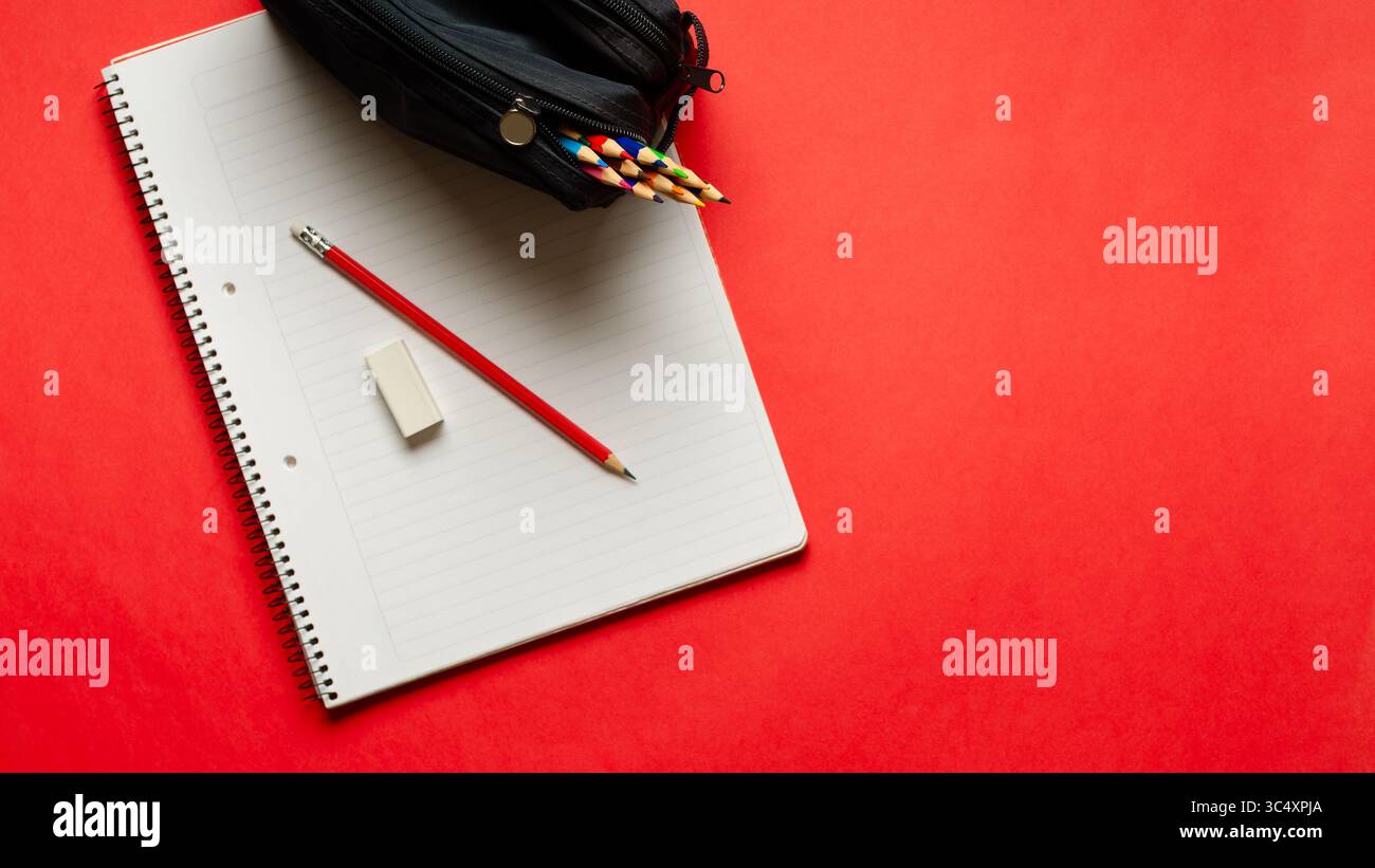 Ein Notizbuch mit Bleistift und Radiergummi und eine Bleistiftetui voller Buntstifte auf rotem Hintergrund und Kopierraum. Back-to-School-Konzept. Stockfoto