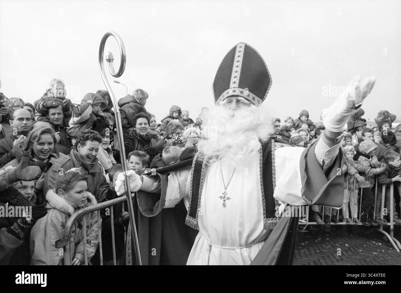Saint Nicholas in IJmuiden, IJmuiden, Niederlande, 19-11-1993 Whizgle News, Dutch Desk, Niederlande, 1950-2000 Eine fröhliche Menschenmenge versammelt sich, um einen festlichen Anlass zu feiern, als eine Figur in raffinierten Gewändern und einem hohen, reich verzierten Hut begrüßt sie mit einem Stab. Kinder und Erwachsene drücken Begeisterung und Freude aus, mit Lächeln und neugierigen Ausdrücken, während sie auf die Ankunft dieser legendären Figur warten. Stockfoto