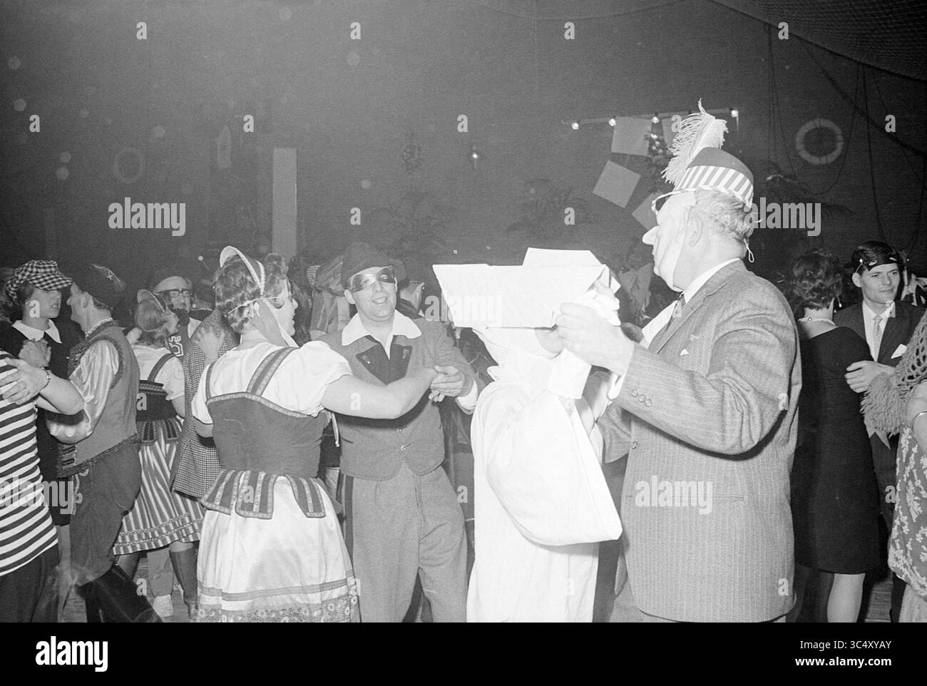 Farbenfroher Abend HST, Hochofen-Schachturnier, 25-01-1968 Whizgle News, Dutch Desk, Niederlande, 1950-2000 Ein lebhaftes Treffen mit Menschen, die in festlichen Kostümen gekleidet sind, tanzen und sich unter Dekorationen amüsieren. Die Atmosphäre ist voller Bewegung und Feiern, während Gäste jeden Alters an der freudigen Veranstaltung teilnehmen. Stockfoto