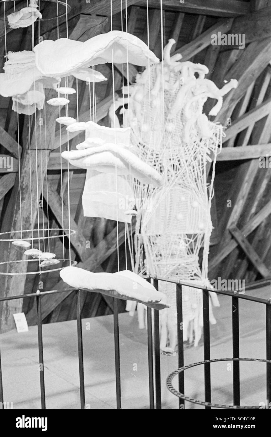 Report on Works in Textiles, Exhibitions, 20-07-1971 Whizgle News, Dutch Desk, Niederlande, 1950-2000 Eine skurrile Ausstellung von hängenden Textilskulpturen mit organischen Formen, die mit feinen Fäden verwoben sind, vor dem Hintergrund komplizierter Holzbalken. Das Arrangement erzeugt ein Gefühl von Bewegung und Leichtigkeit und lädt die Zuschauer ein, das Zusammenspiel von Textur und Form zu erforschen. Stockfoto