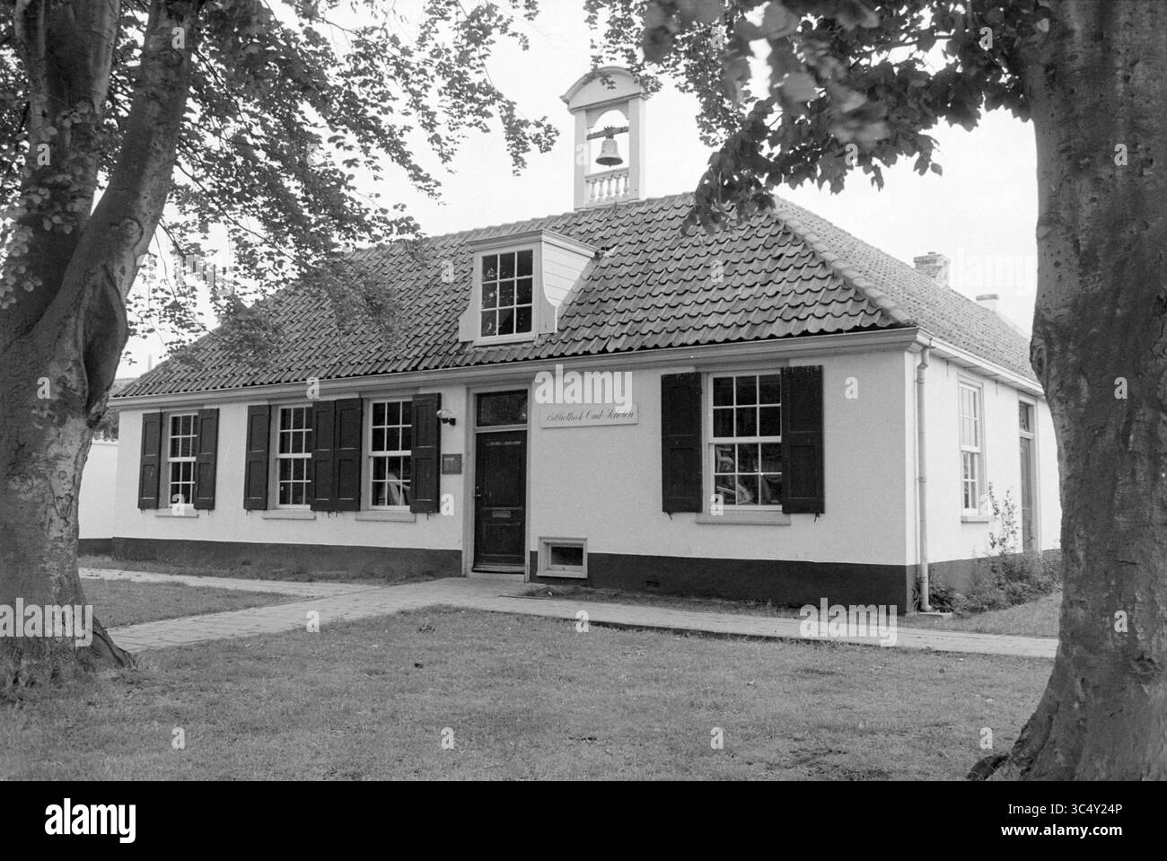 Außenbibliothek Oud Schoten Vergierdeweg, Haarlem, Vergierdeweg, The Netherlands Whizgle News, Dutch Desk, Niederlande, 1950-2000 Ein bezauberndes Gebäude mit Giebeldach und ikonischem Glockenturm, eingerahmt von hohen Bäumen, verfügt über große, verschlossene Fenster und einen einladenden Eingang. Der historische Charakter des Gebäudes wird durch seine traditionellen architektonischen Details und die gut gepflegte Anlage hervorgehoben. Stockfoto
