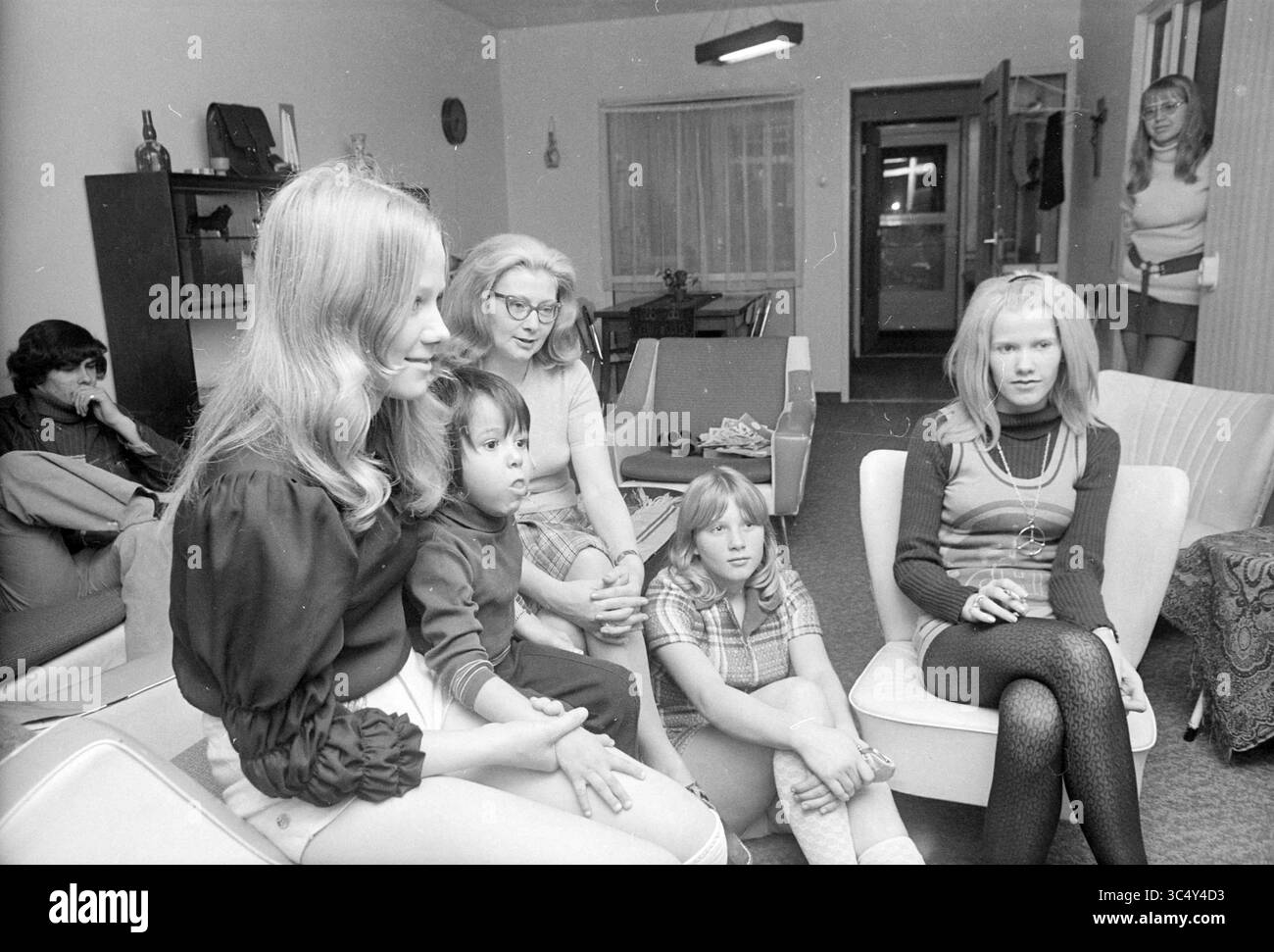 Familie bei TV Gandhistraat 147, Familien, 09-12-1971 Whizgle News, Dutch Desk, Niederlande, 1950-2000 Eine Gruppe von sechs Personen versammelt sich in einem gemütlichen Wohnzimmer. Vier Frauen sitzen und unterhalten sich, während ein Kind neben einer von ihnen sitzt. Die Atmosphäre ist lässig, mit Möbeln und Dekor, die einen Stil der Mitte des Jahrhunderts widerspiegeln. Im Hintergrund entspannt sich ein Mann, der die entspannte Atmosphäre des Treffens verstärkt. Stockfoto