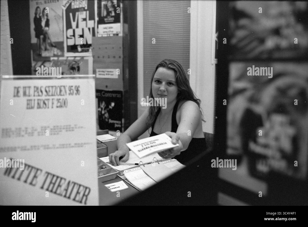 Freiwillige Wendy, Witte Theater, IJmuiden, IJmuiden, Kanaalstraat, Niederlande, 19-09-1995 Whizgle News, Dutch Desk, Niederlande, 1950-2000 Eine junge Frau an einem Ticketschalter hält ein Ticket, während sie von Plakaten für verschiedene Shows umgeben ist, die die lebhafte Atmosphäre eines Theaters zeigen. Stockfoto