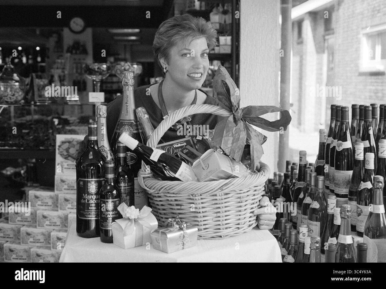 Beers, Wijnkoperij Heemstede, Heemstede, Niederlande, 18-08-1993 Whizgle News, Dutch Desk, Niederlande, 1950-2000 Eine fröhliche Frau steht in einem Geschäft, gefüllt mit verschiedenen Flaschen und einem großen Geschenkkorb mit einer Schleife, in dem eine Auswahl an Getränken und festlichen Geschenken präsentiert wird. Stockfoto