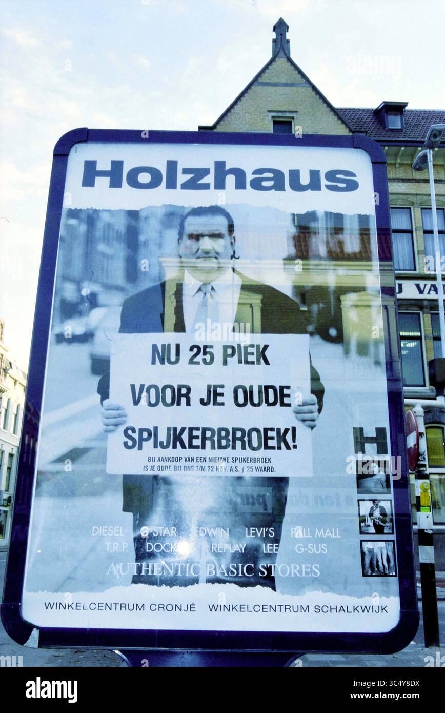 Werbung aus dem Bekleidungsgeschäft Holzhaus Gen. Cronjestraat, Haarlem, Generaal Cronjéstraat, Niederlande, 14-11-2001 Whizgle News, Dutch Desk, Niederlande, 1950-2000 Eine große Werbung zeigt einen Mann, der ein Schild mit der Aufschrift „NOW 25 MÄUSE FOR YOUR OLD HOSES!“ hält. Werbung für ein Bekleidungsgeschäft. Der Hintergrund umfasst verschiedene Bekleidungsmarken und ist von urbanen Elementen umgeben, die auf ein Einkaufsviertel hindeuten. Stockfoto