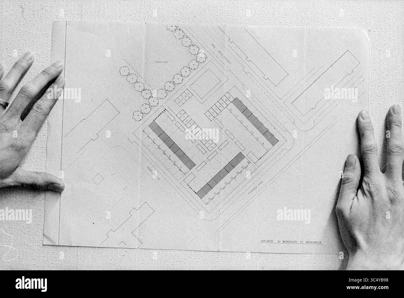 Karte von 24 neuen Häusern in Beverwijk, Beverwijk, Fokkerlaan, Niederlande, 00-11-1970 Whizgle News, Dutch Desk, Niederlande, 1950-2000 Es wird Ein Grundriss angezeigt, der die Anordnung von Gebäuden, Wegen und Grünflächen innerhalb eines ausgewiesenen Bereichs zeigt. Hände halten die Kanten des Plans und betonen seine Bedeutung als Leitfaden für die Entwicklung. Stockfoto