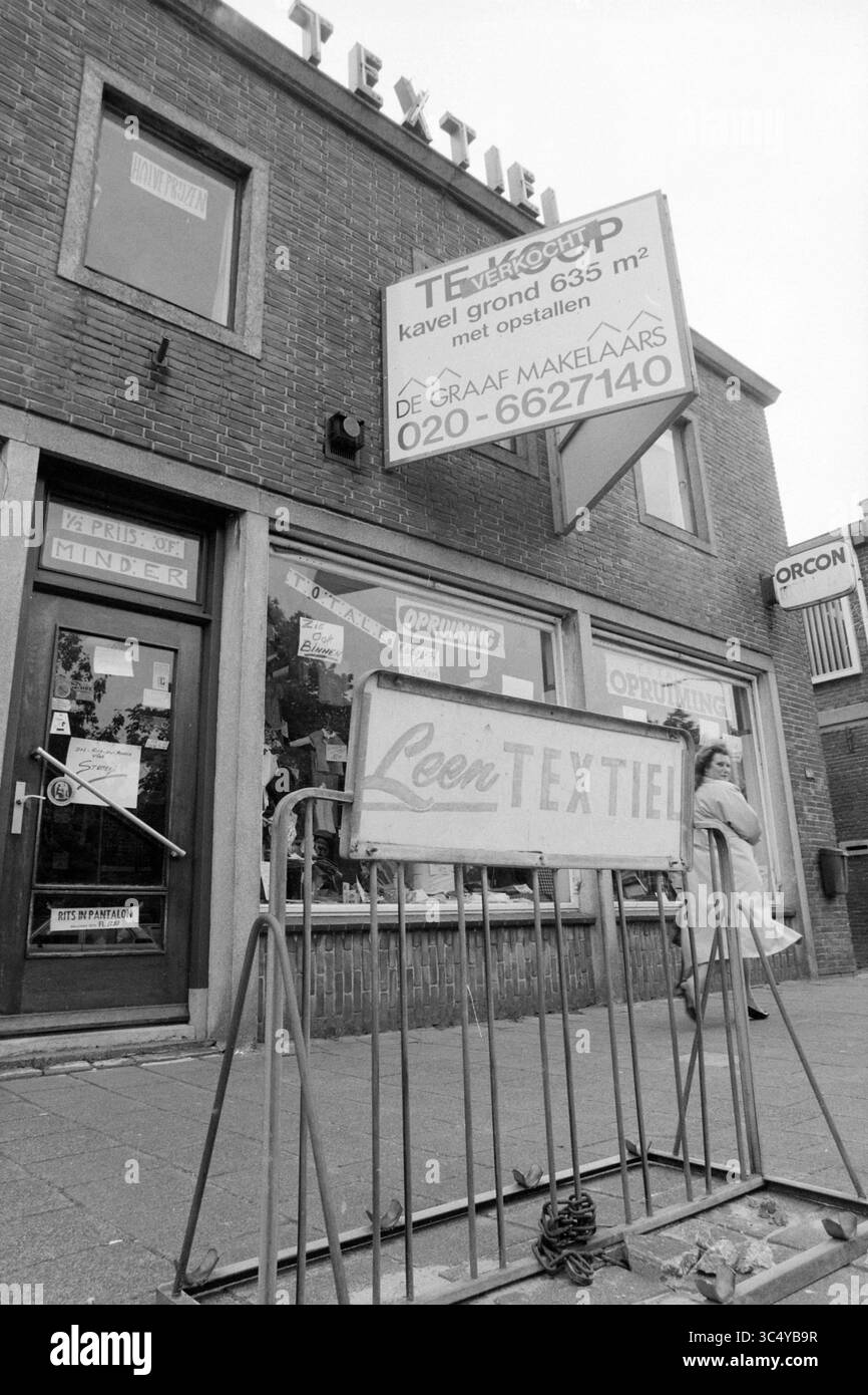 Außenansicht Leen Textiel in Hoofddorp, Hoofddorp, Niederlande, 19-06-1991 Whizgle News, Dutch Desk, Niederlande, 1950-2000 Eine Ladenfront, in der das Wort „TEXTIEL“ deutlich sichtbar erscheint, mit einem Schild, das die Größe und die Kontaktinformationen der Immobilien angibt. Der Eingang ist mit Glastüren ausgestattet, und eine Person wird beim Vorbeigehen gesehen, was der städtischen Szene ein Gefühl von Leben verleiht. Die Architektur des Gebäudes spiegelt eine Mischung aus modernem Geschäftsdesign und praktischer Funktionalität wider. Stockfoto