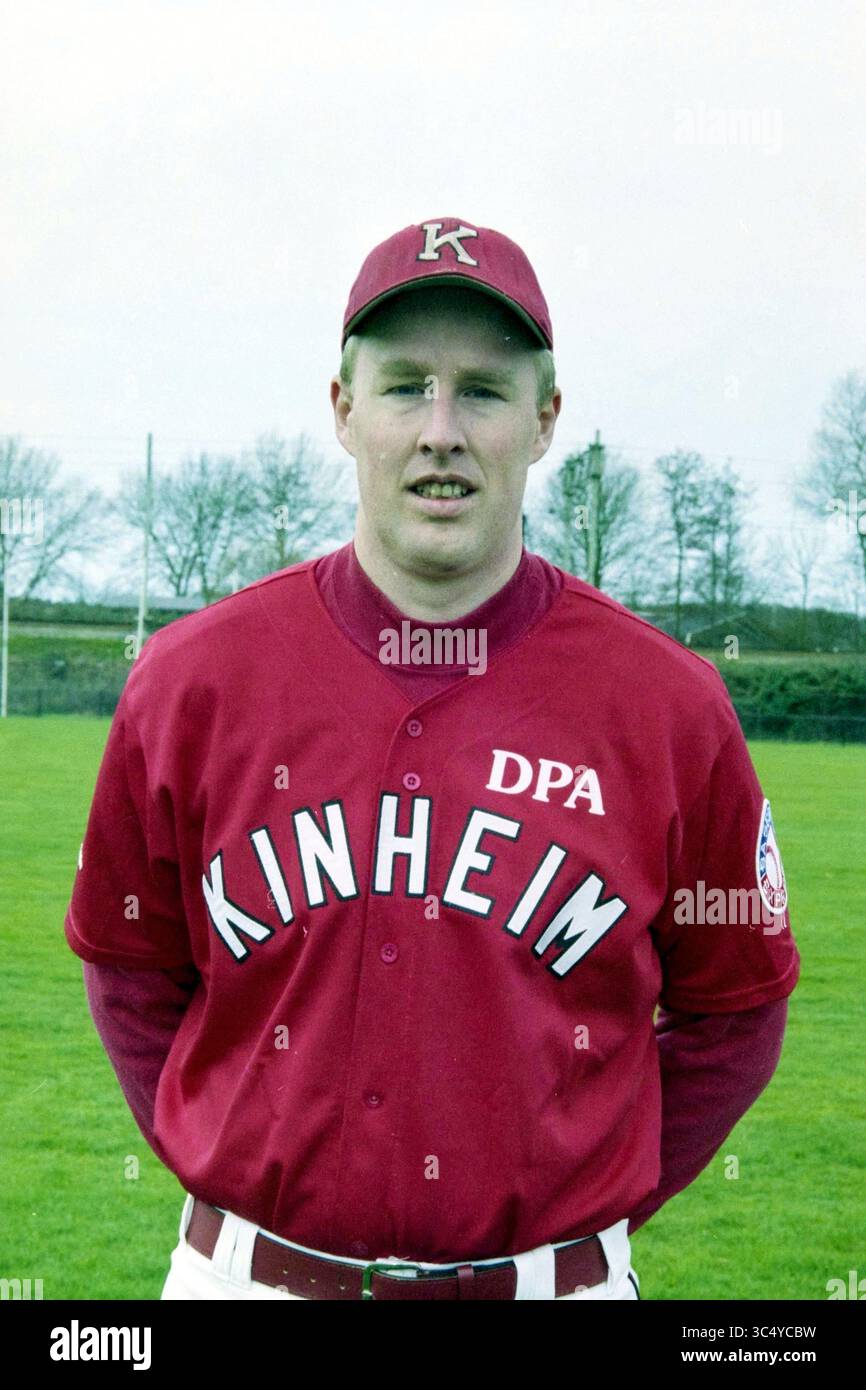 Head Players Kinheim + Board, 11-03-2000 Whizgle News, Dutch Desk, Niederlande, 1950-2000 Ein Spieler steht stolz auf dem Baseballfeld, gekleidet in einer roten Uniform mit dem Namen „KINHEIM“ und den Buchstaben „DPA“. Mit einer Kappe, die den Buchstaben „K“ trägt, lächelt er selbstbewusst und bereit für das bevorstehende Spiel. Das üppige grüne Gras umgibt ihn und hebt die lebendigen Farben seines Teams hervor. Stockfoto