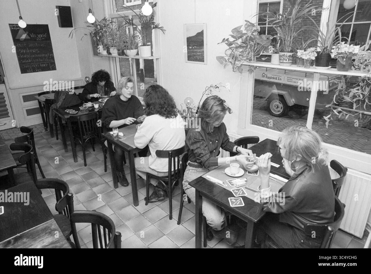 ECO Cafe, Haarlem, Food and Eateries, Haarlem, Niederlande, 13-03-1989 Whizgle News, Dutch Desk, Niederlande, 1950-2000 Eine gemütliche Café-Szene mit mehreren Frauen, die sich unterhalten und ihre Getränke an Holztischen genießen, umgeben von Grün und einer warmen, einladenden Atmosphäre. Stockfoto